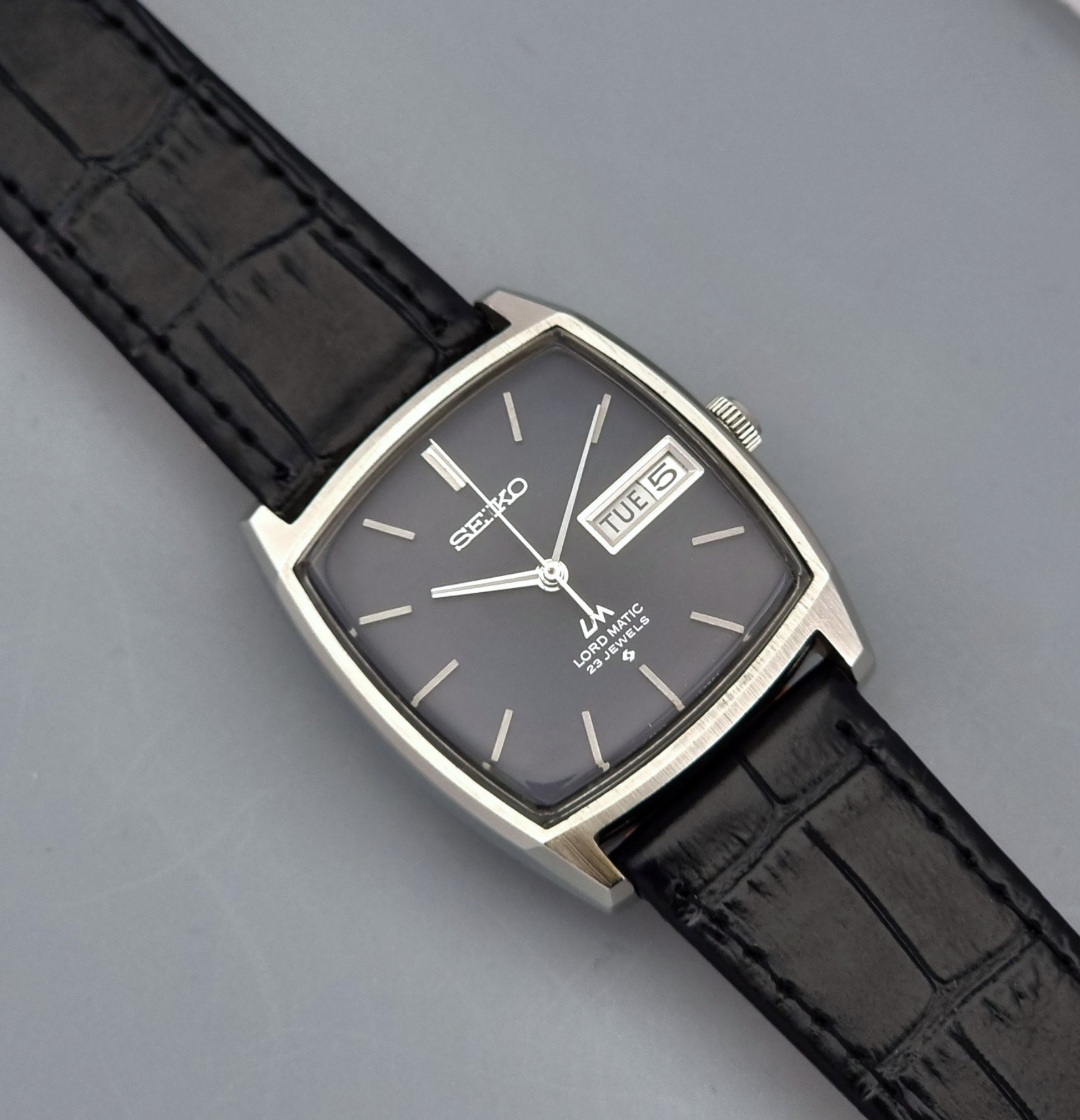 Vintage Seiko Lord Matic watch with black leather strap and gray face on a gray background