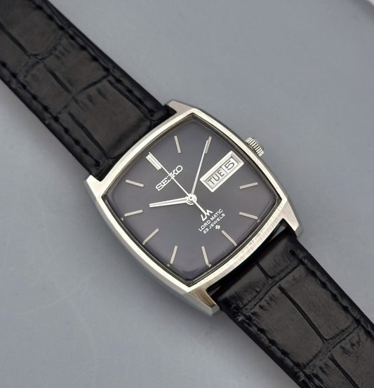 Vintage Seiko Lord Matic watch with black leather strap and gray face on a gray background
