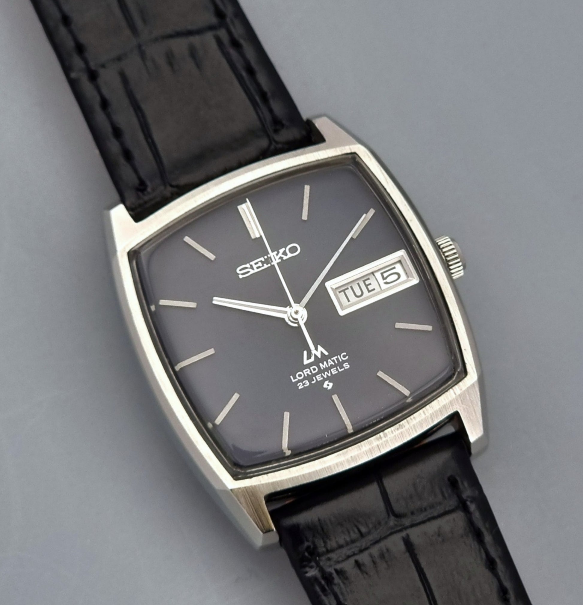 Vintage Seiko Lord Matic watch with black leather strap on a gray background