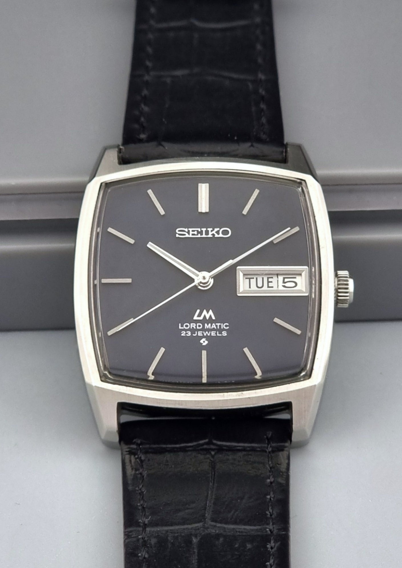 Vintage Seiko Lord Matic watch with black leather strap on a gray background