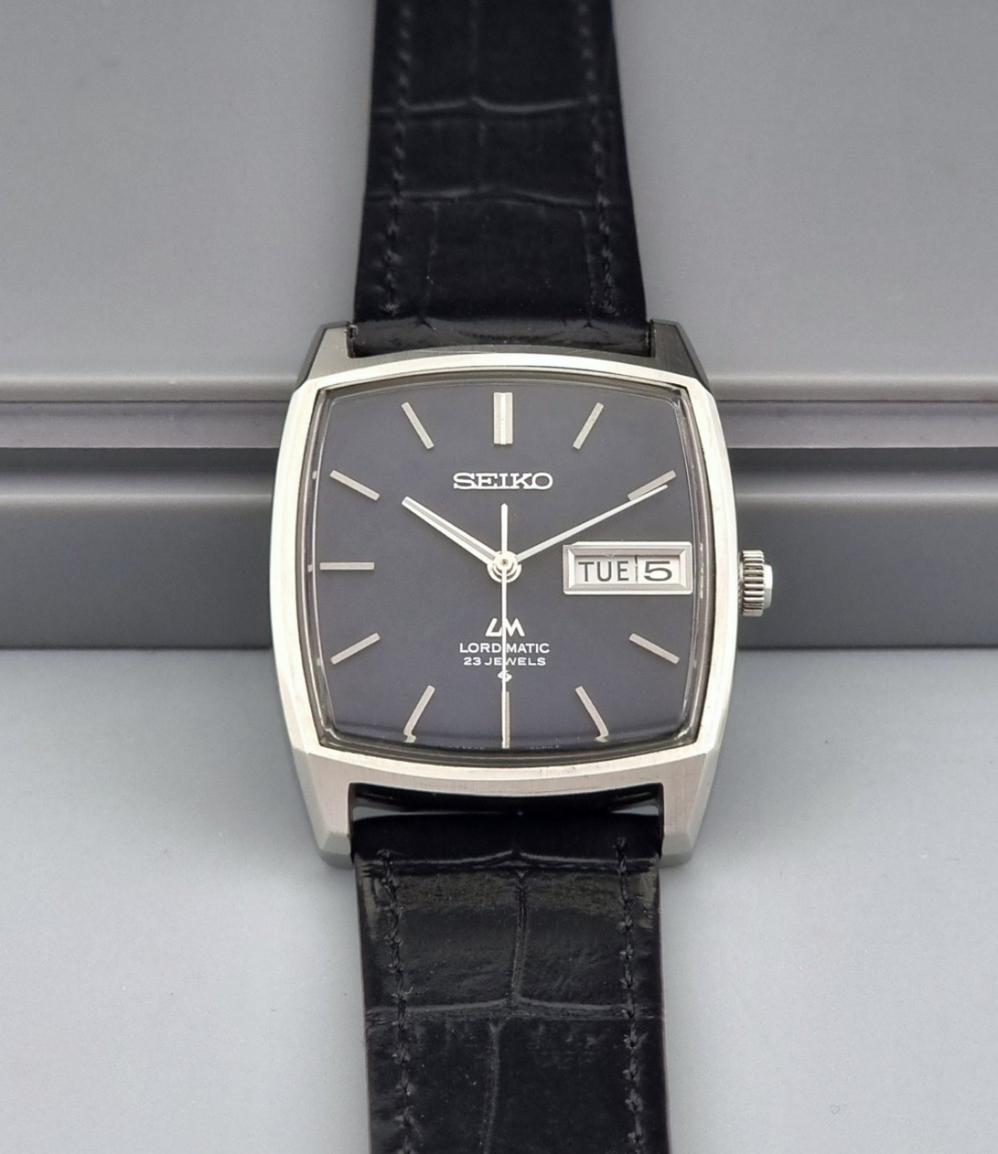 Vintage Seiko Lord Matic watch with black leather strap on a gray background