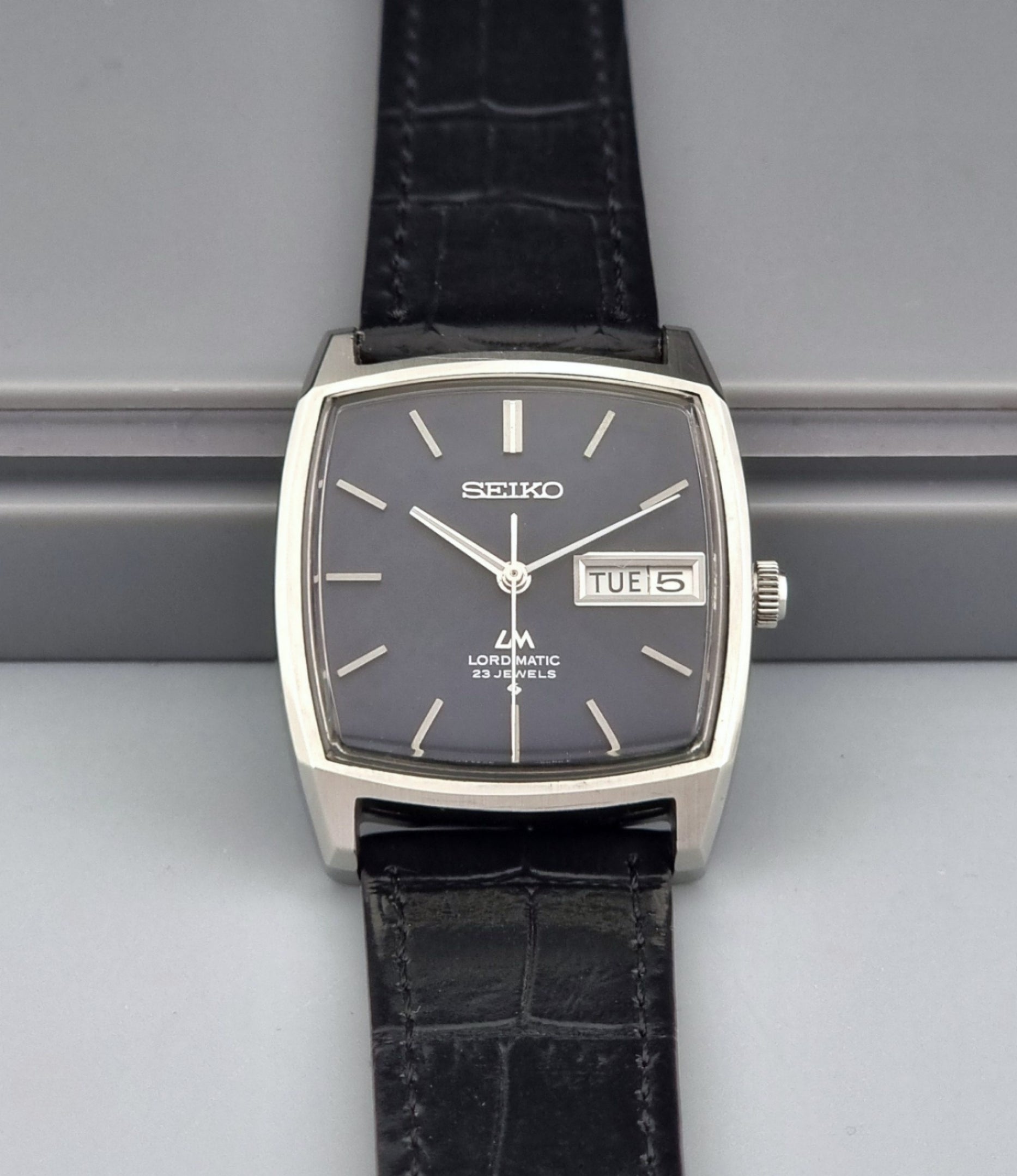 Vintage Seiko Lord Matic watch with black leather strap on a gray background