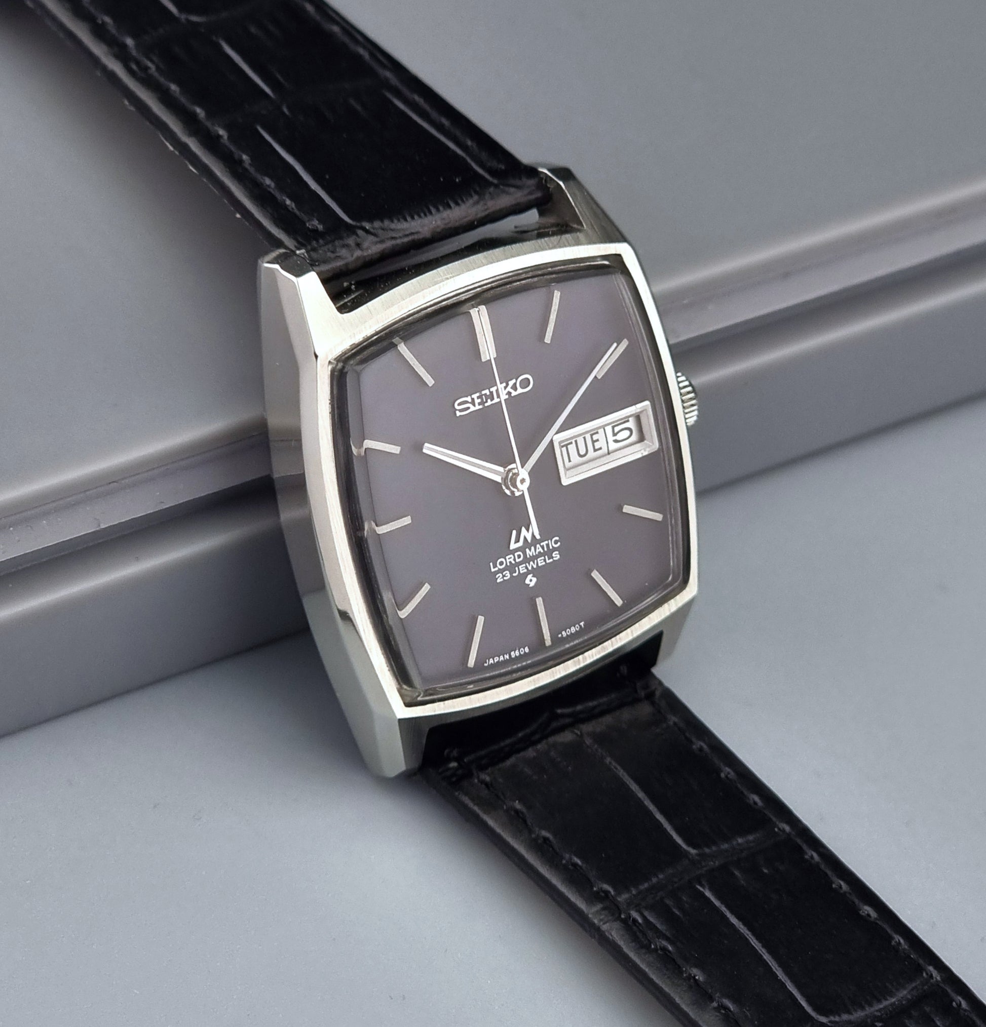 Vintage Seiko watch with black leather strap on a gray surface