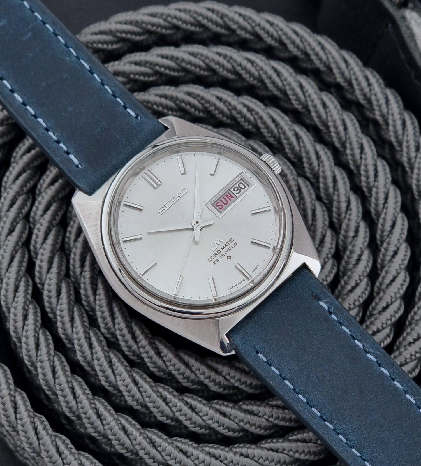 Vintage Seiko Wristwatch LordMatic 5606-7000 with blue strap on a textured gray background