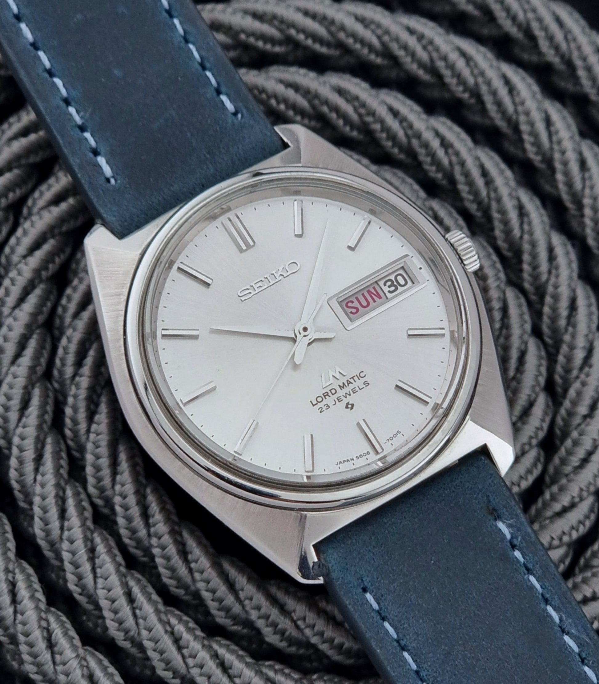 Vintage Seiko Wristwatch LordMatic 5606-7000 with blue strap on a textured gray background close front view