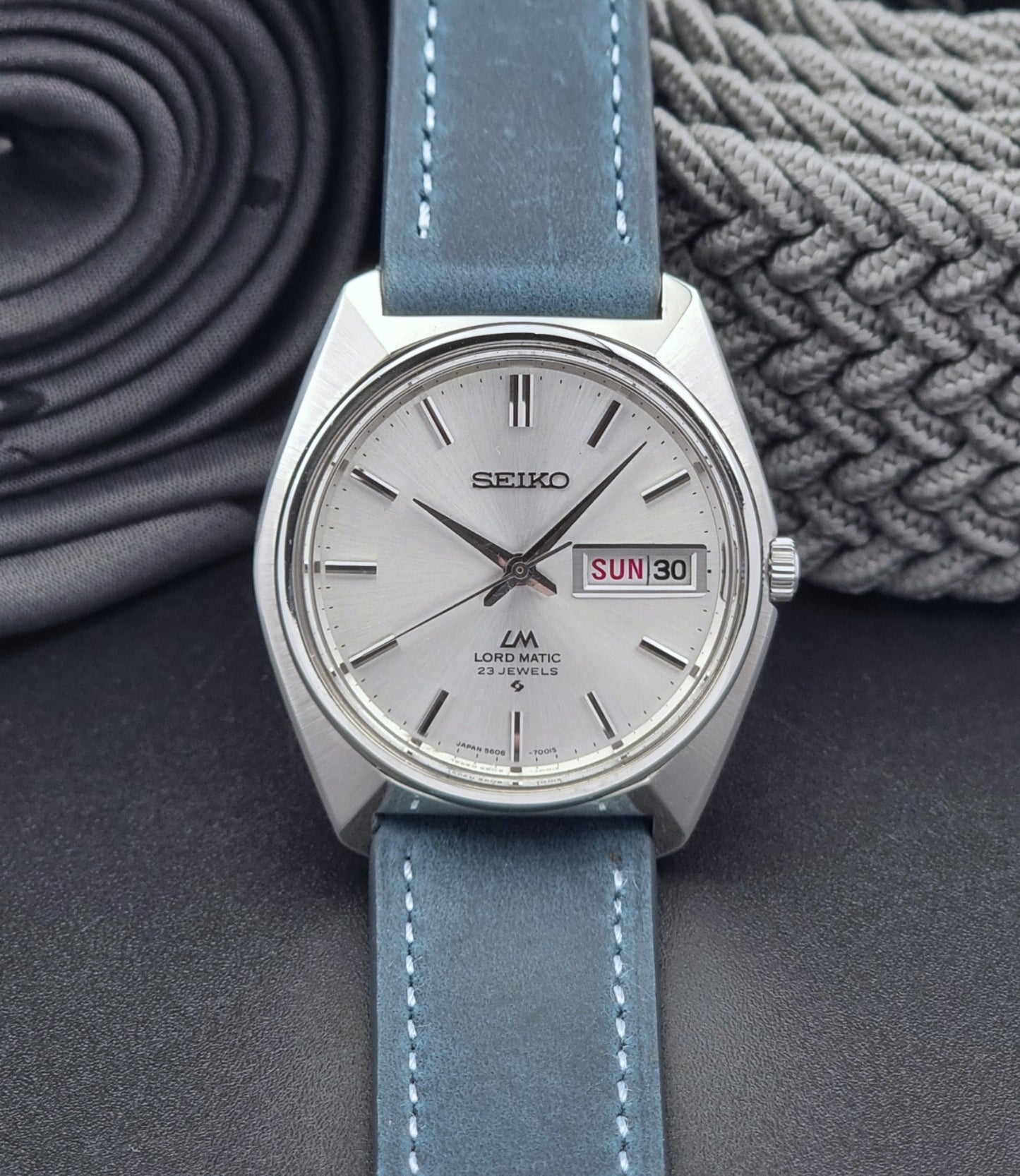 Vintage Seiko Wristwatch LordMatic 5606-7000 with blue strap on a textured gray background front