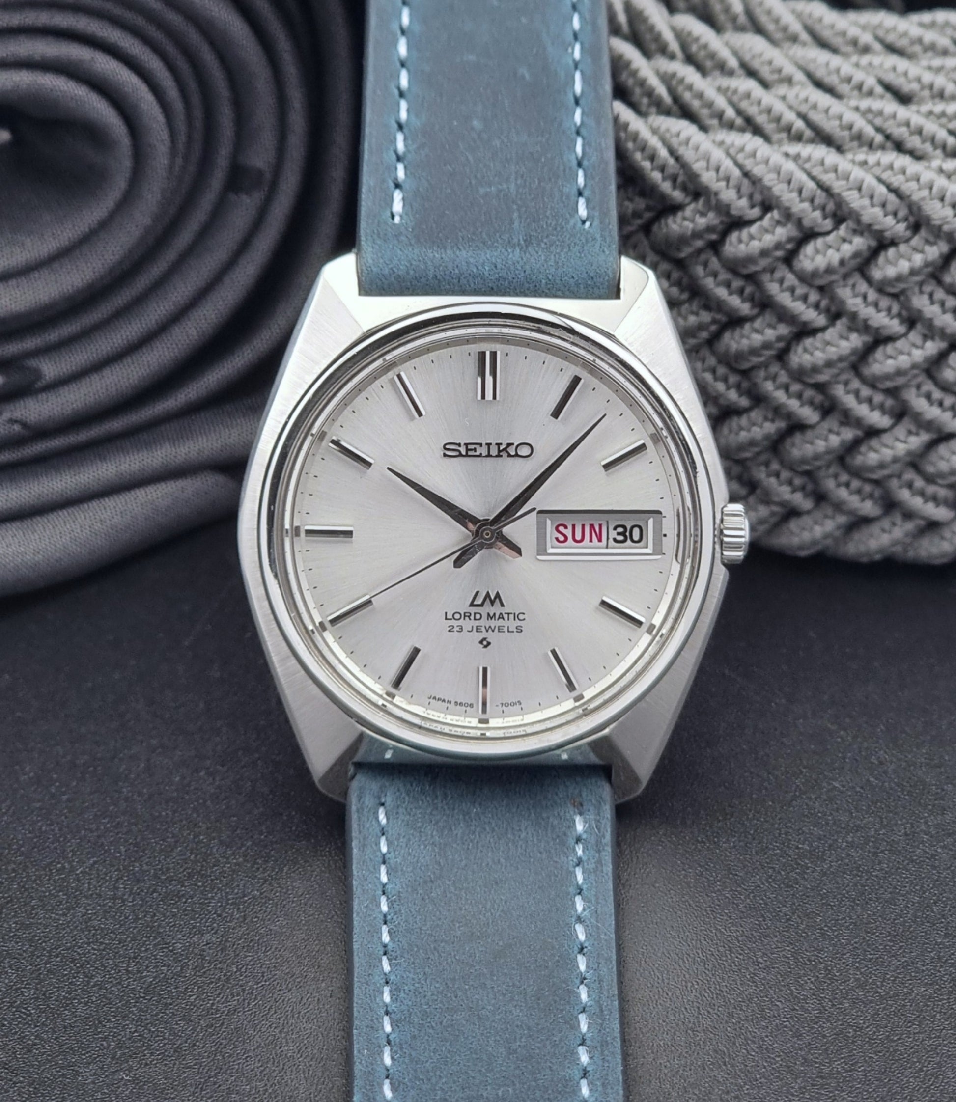 Vintage Seiko Wristwatch LordMatic 5606-7000 with blue strap on a textured gray background front