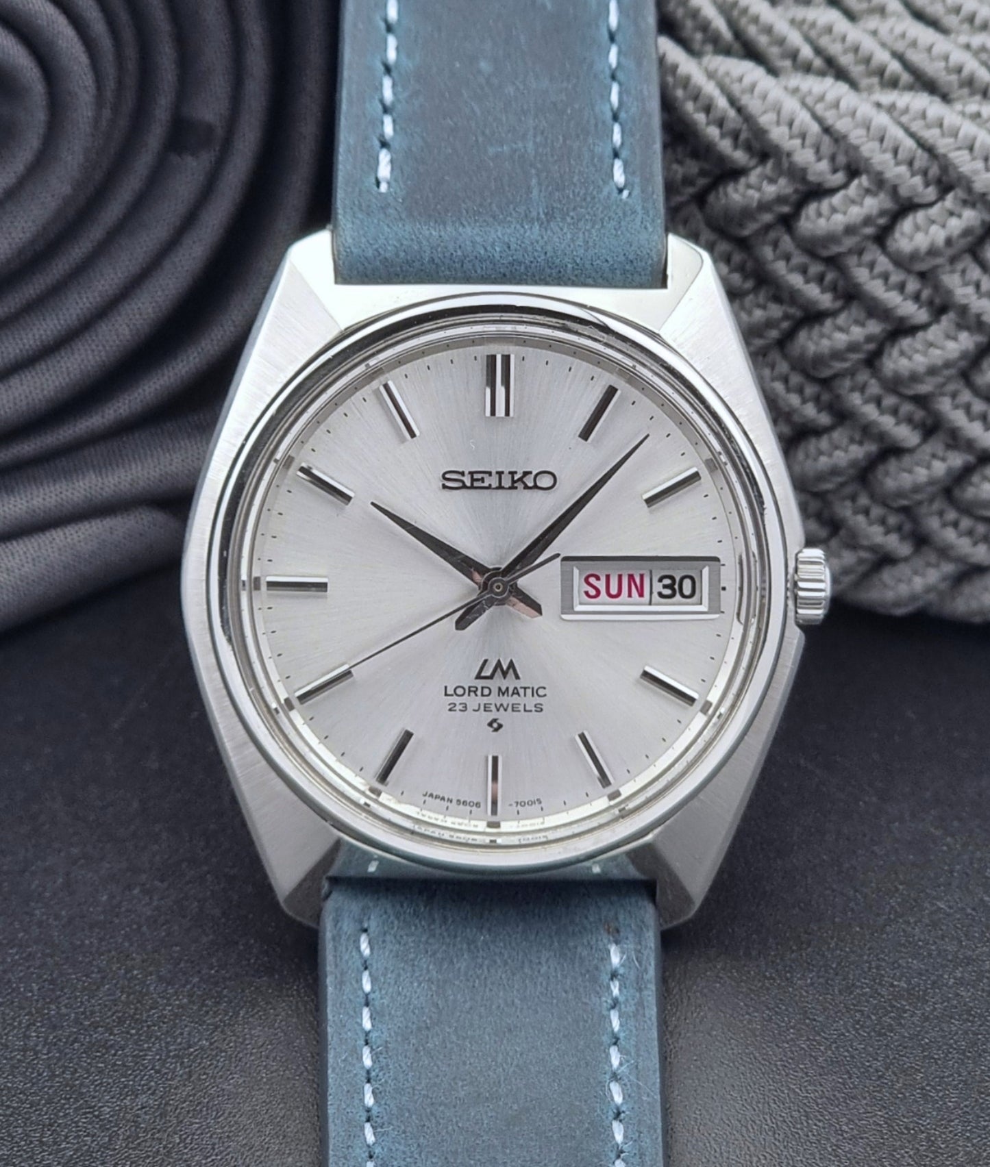 Vintage Seiko Wristwatch LordMatic 5606-7000 with blue strap on a textured gray background close front view