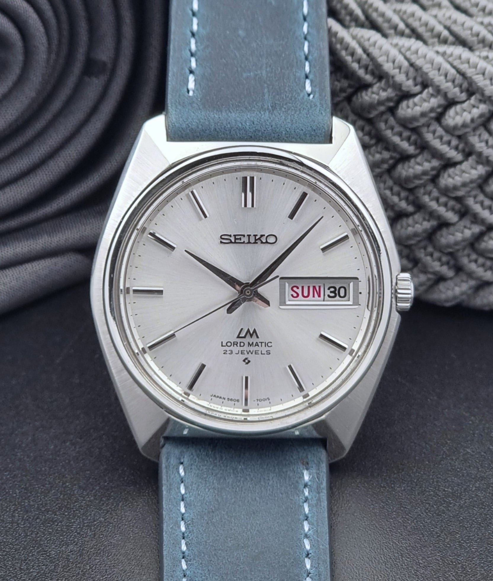 Vintage Seiko Wristwatch LordMatic 5606-7000 with blue strap on a textured gray background close front view