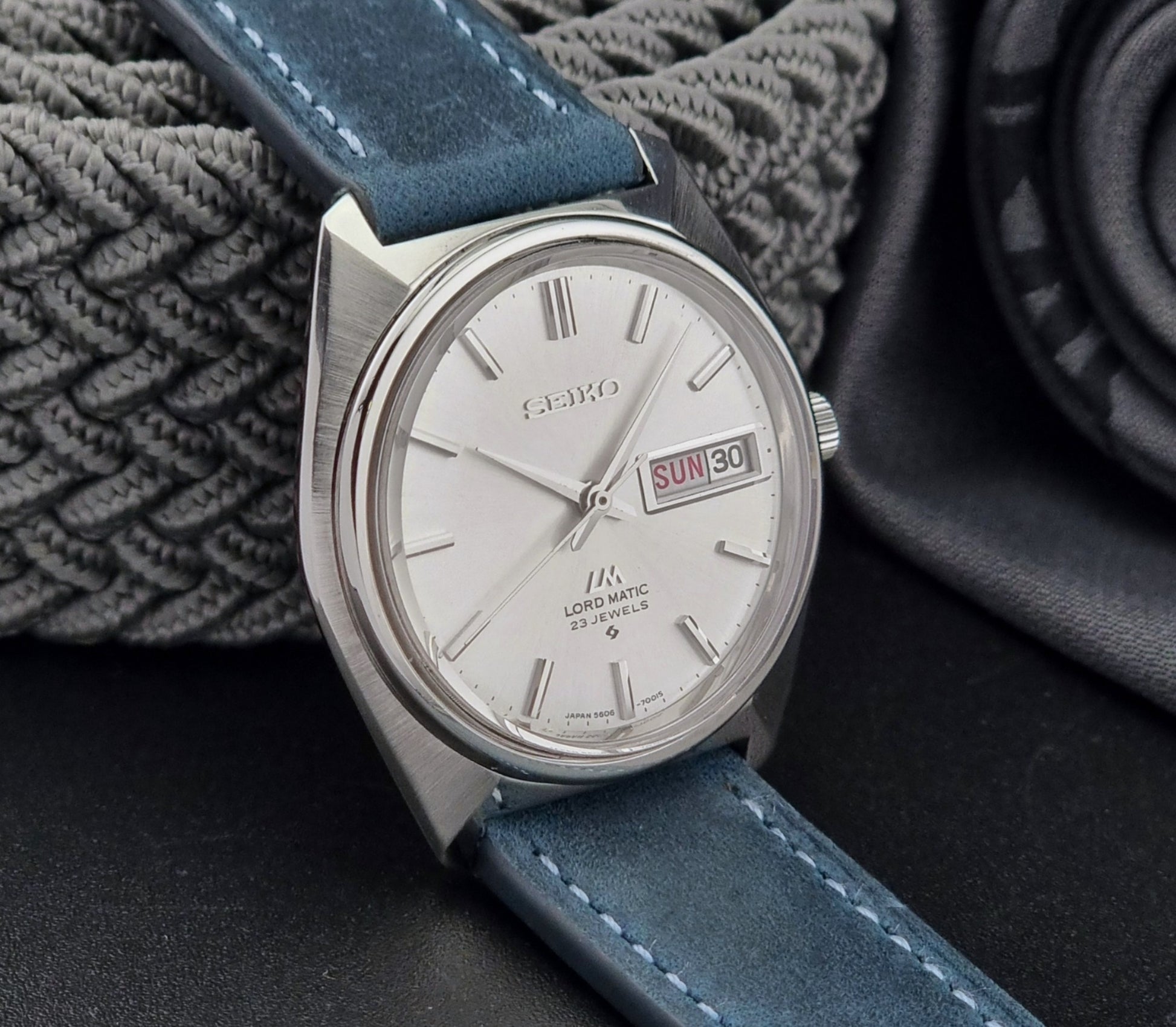 Vintage Seiko Wristwatch LordMatic 5606-7000 with blue strap on a textured gray background side view