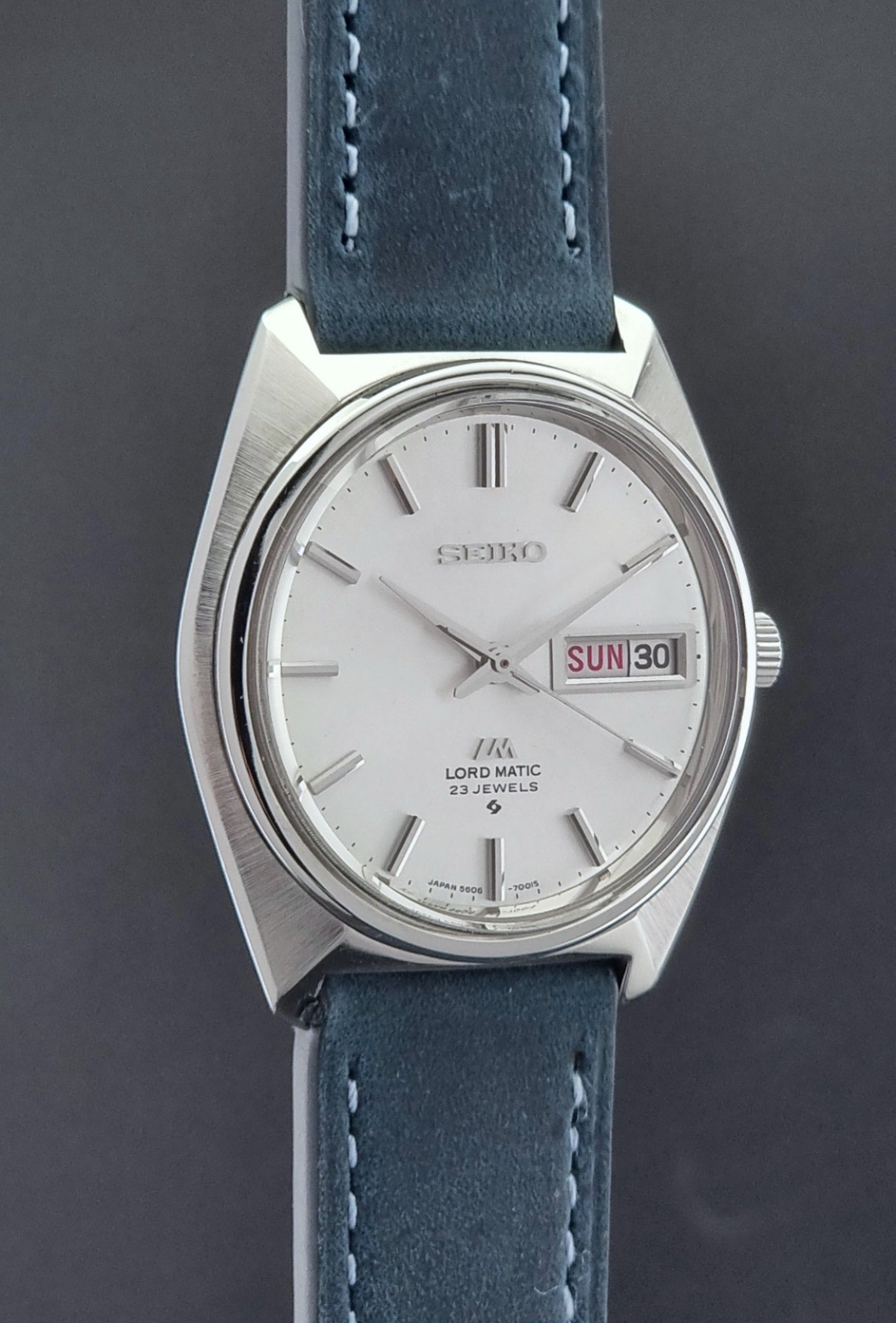 Vintage Seiko Wristwatch LordMatic 5606-7000 with blue strap on a textured gray background side profile