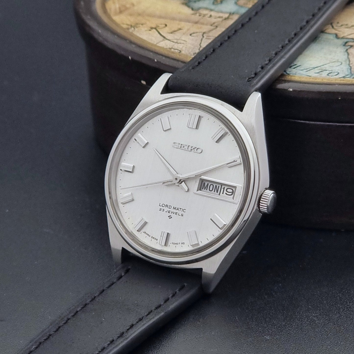 Vintage Seiko Wristwatch LordMatic 5606-7040 with black leather strap on a dark surface crown view