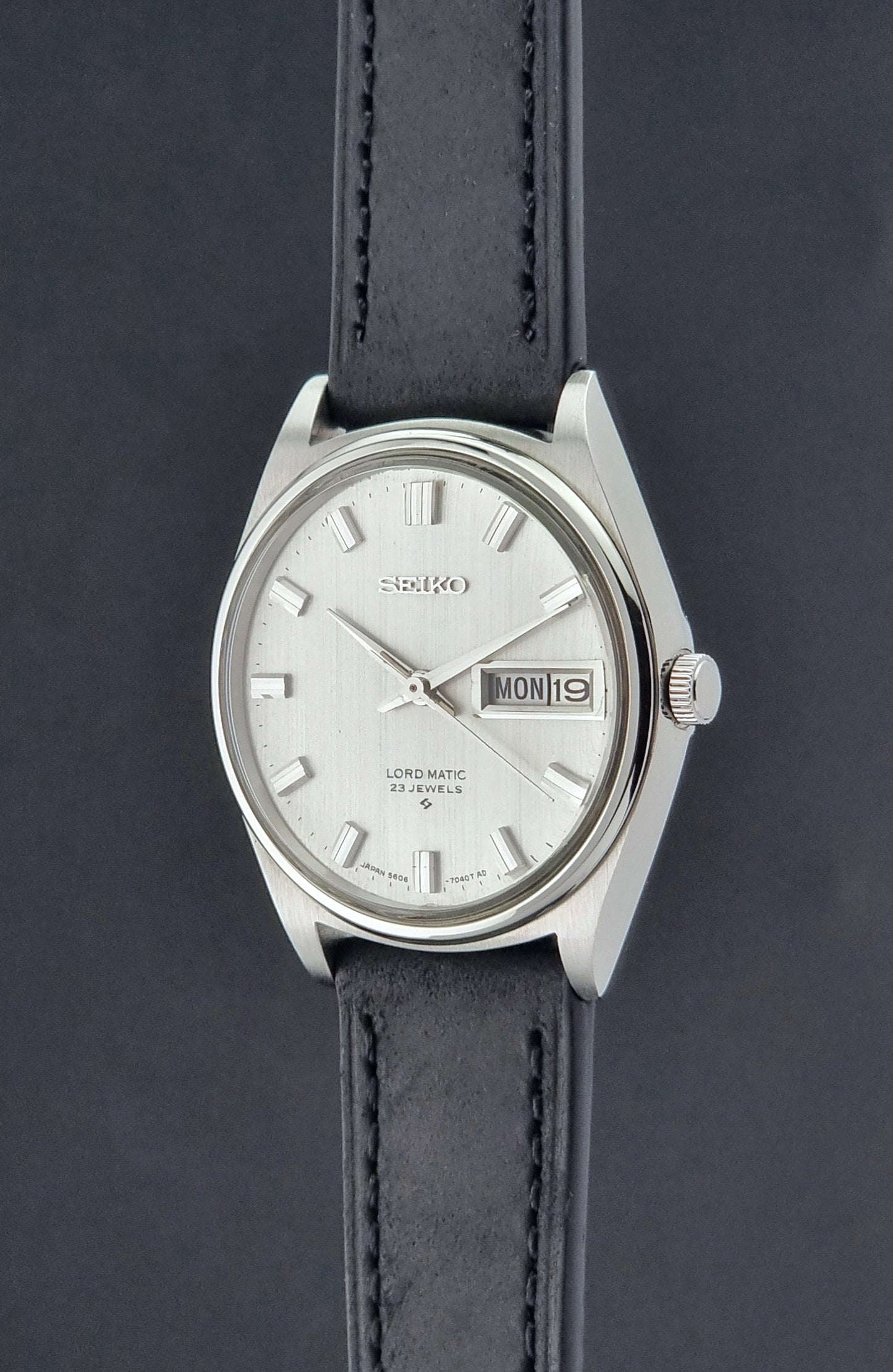 Vintage Seiko Wristwatch LordMatic 5606-7040 with black leather strap on a dark surface crown profile view