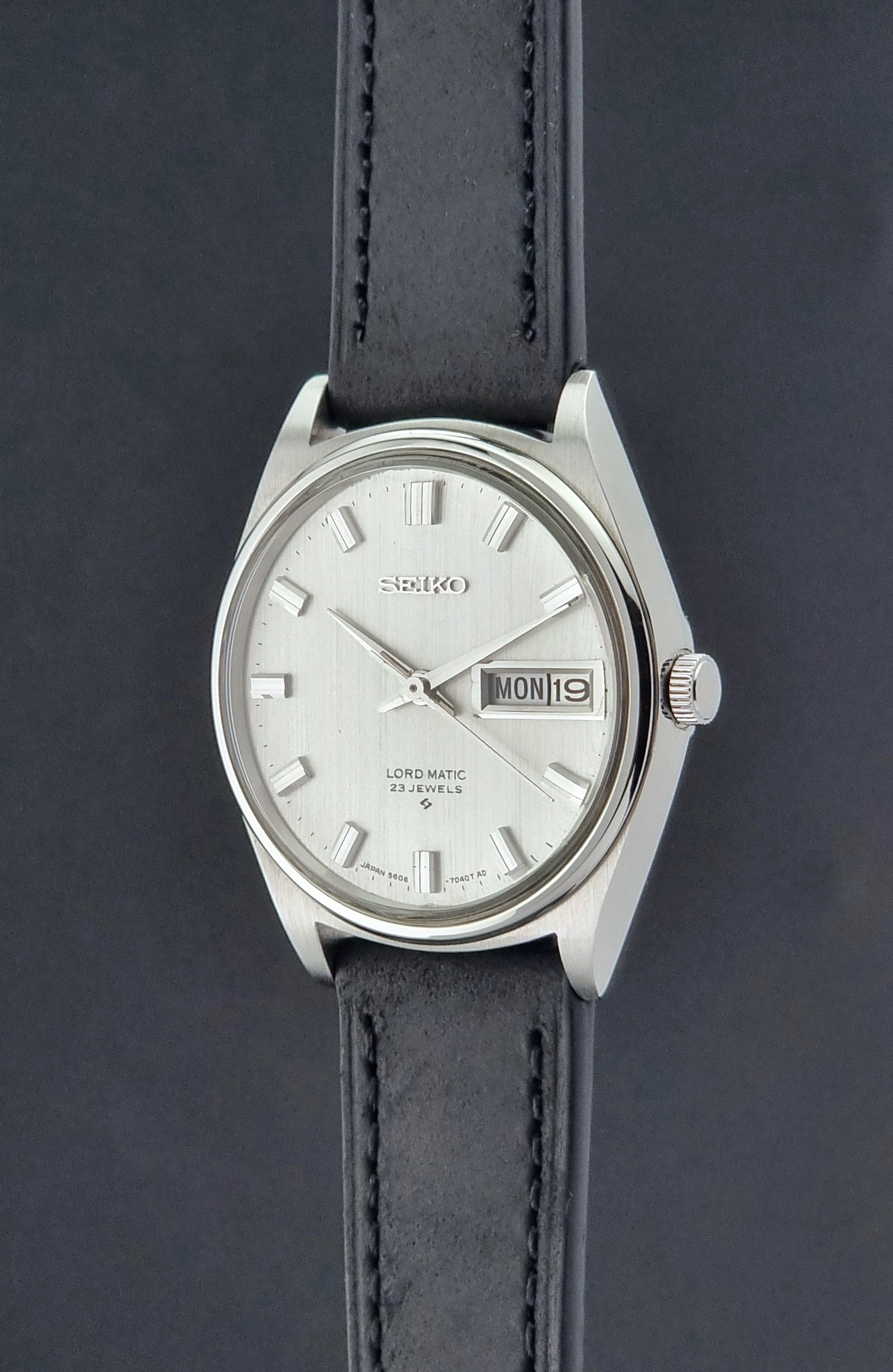 Vintage Seiko Wristwatch LordMatic 5606-7040 with black leather strap on a dark surface crown profile view