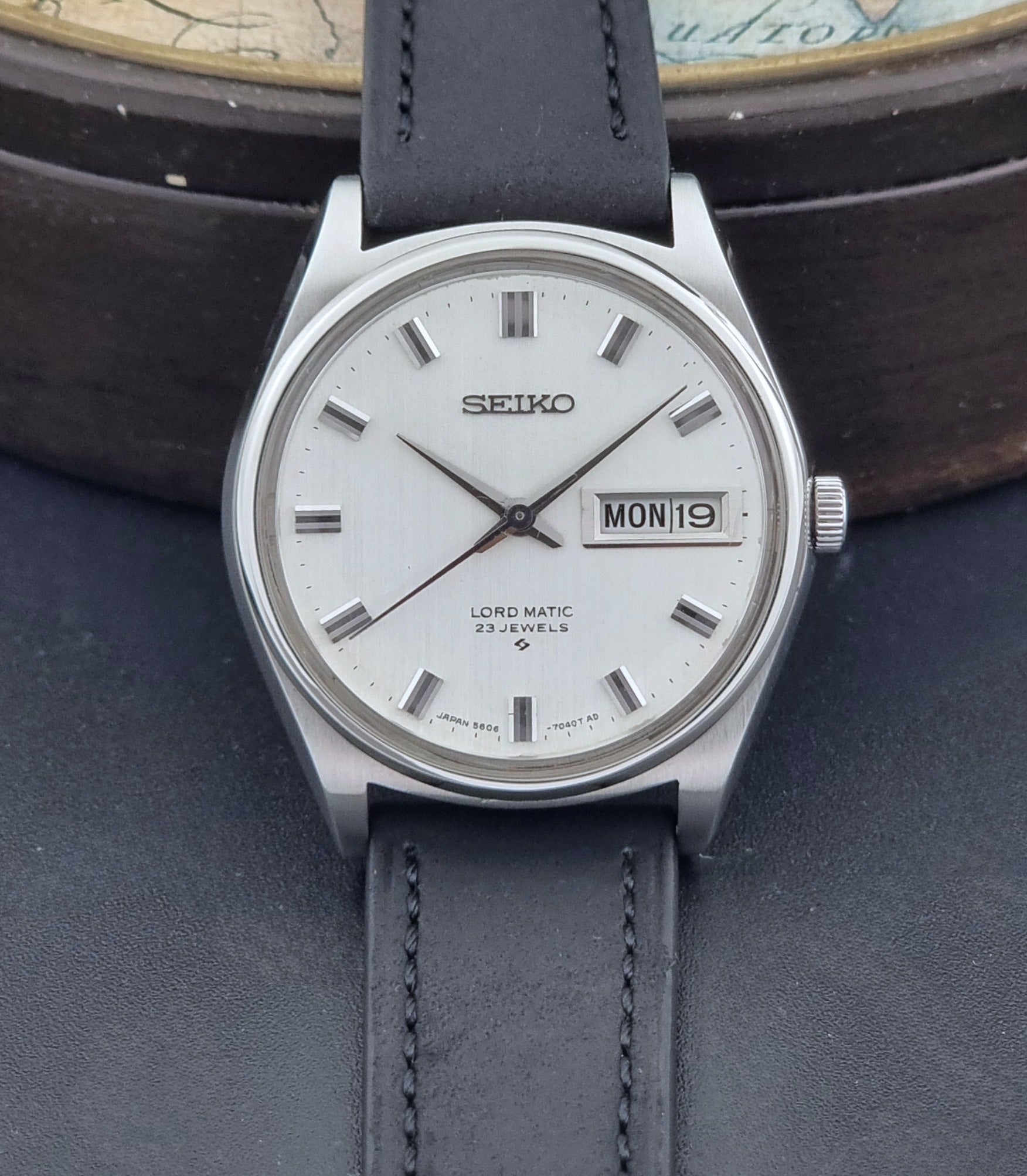 Vintage Seiko Wristwatch LordMatic 5606-7040 with black leather strap on a dark surface dial view