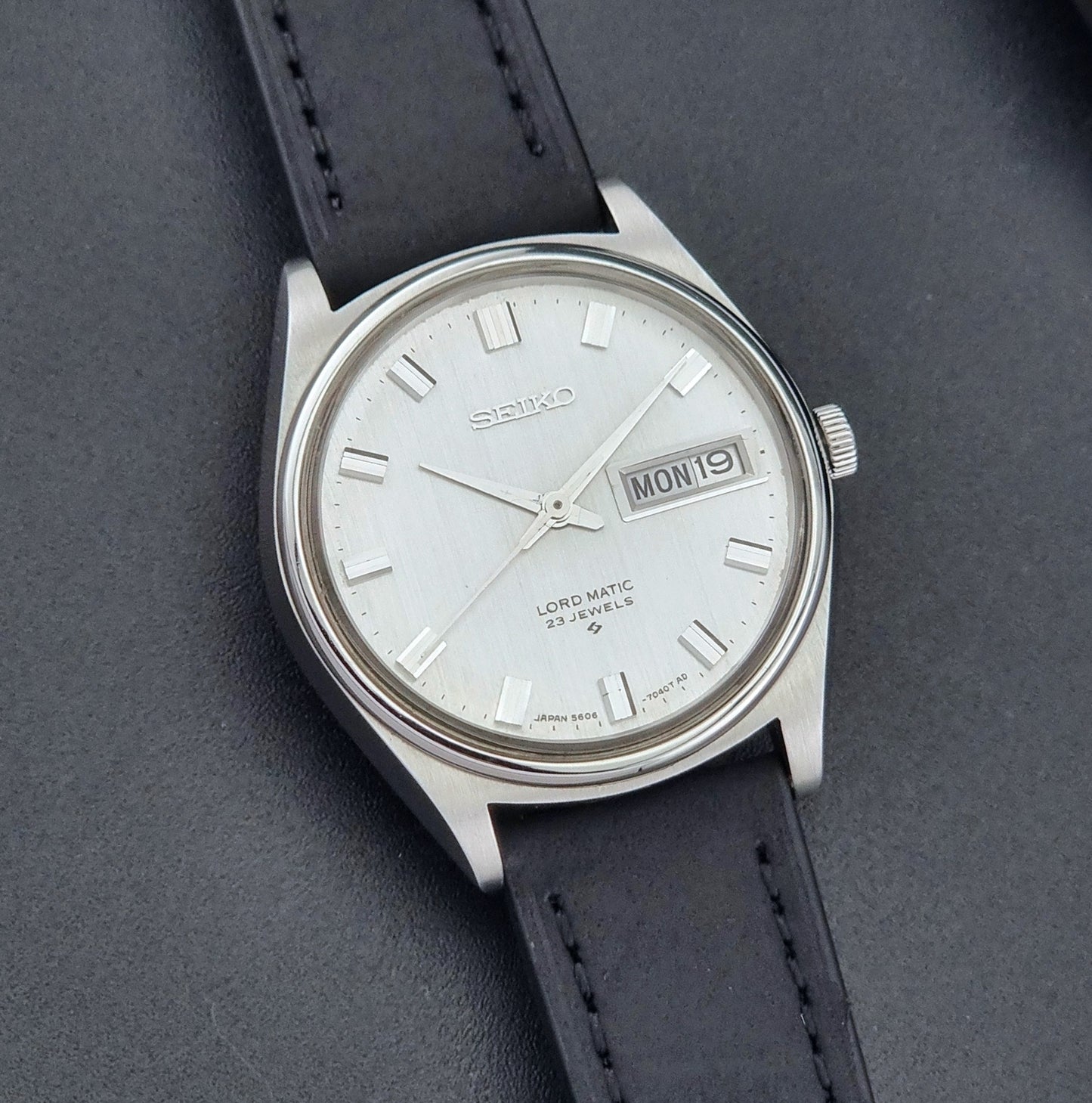 Vintage Seiko Wristwatch LordMatic 5606-7040 with black leather strap on a dark surface front view