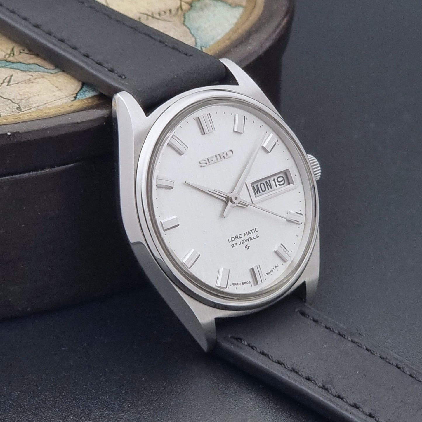 Vintage Seiko Wristwatch LordMatic 5606-7040 with black leather strap on a dark surface side view