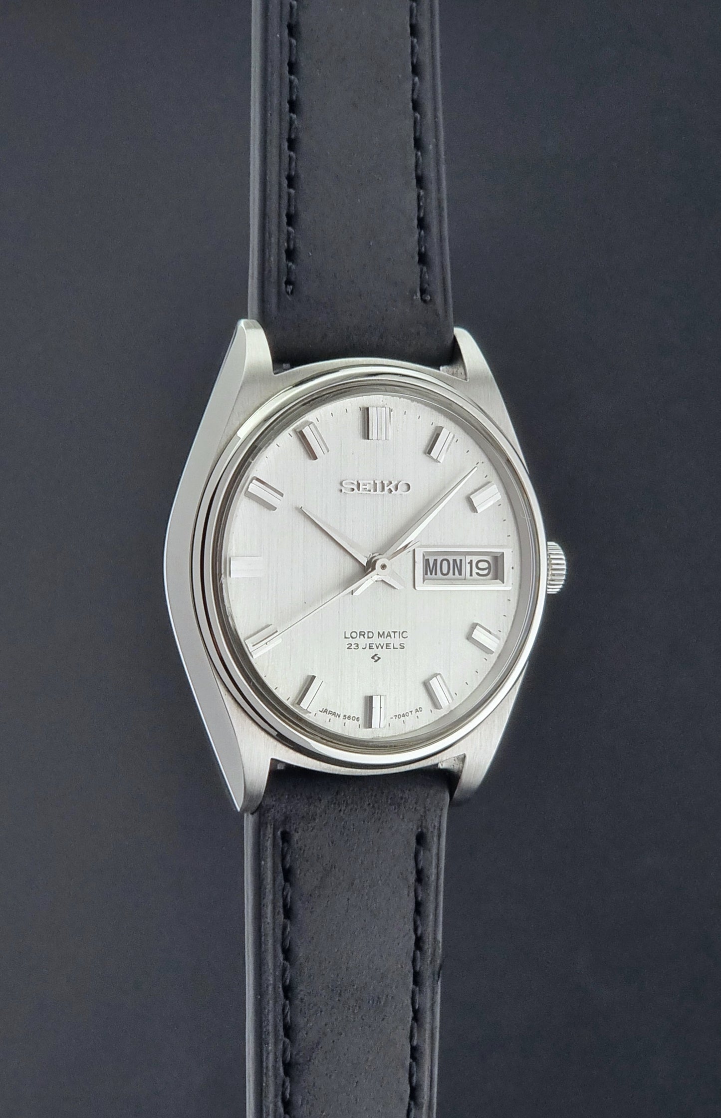 Vintage Seiko Wristwatch LordMatic 5606-7040 with black leather strap on a dark surface side profile view