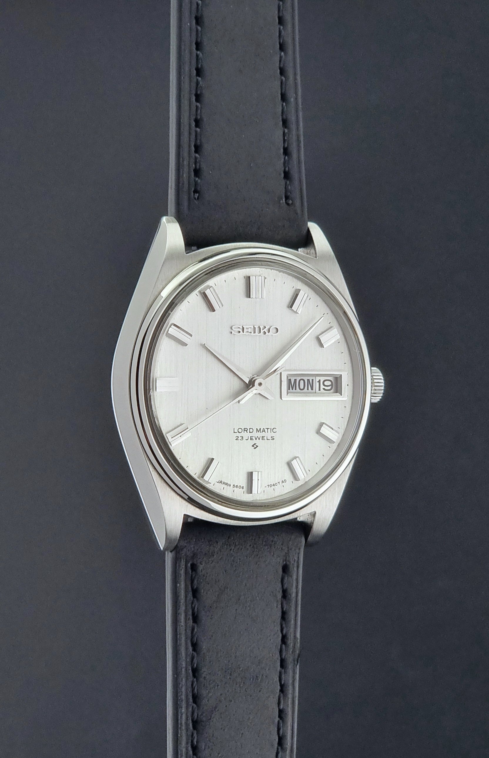 Vintage Seiko Wristwatch LordMatic 5606-7040 with black leather strap on a dark surface side profile view