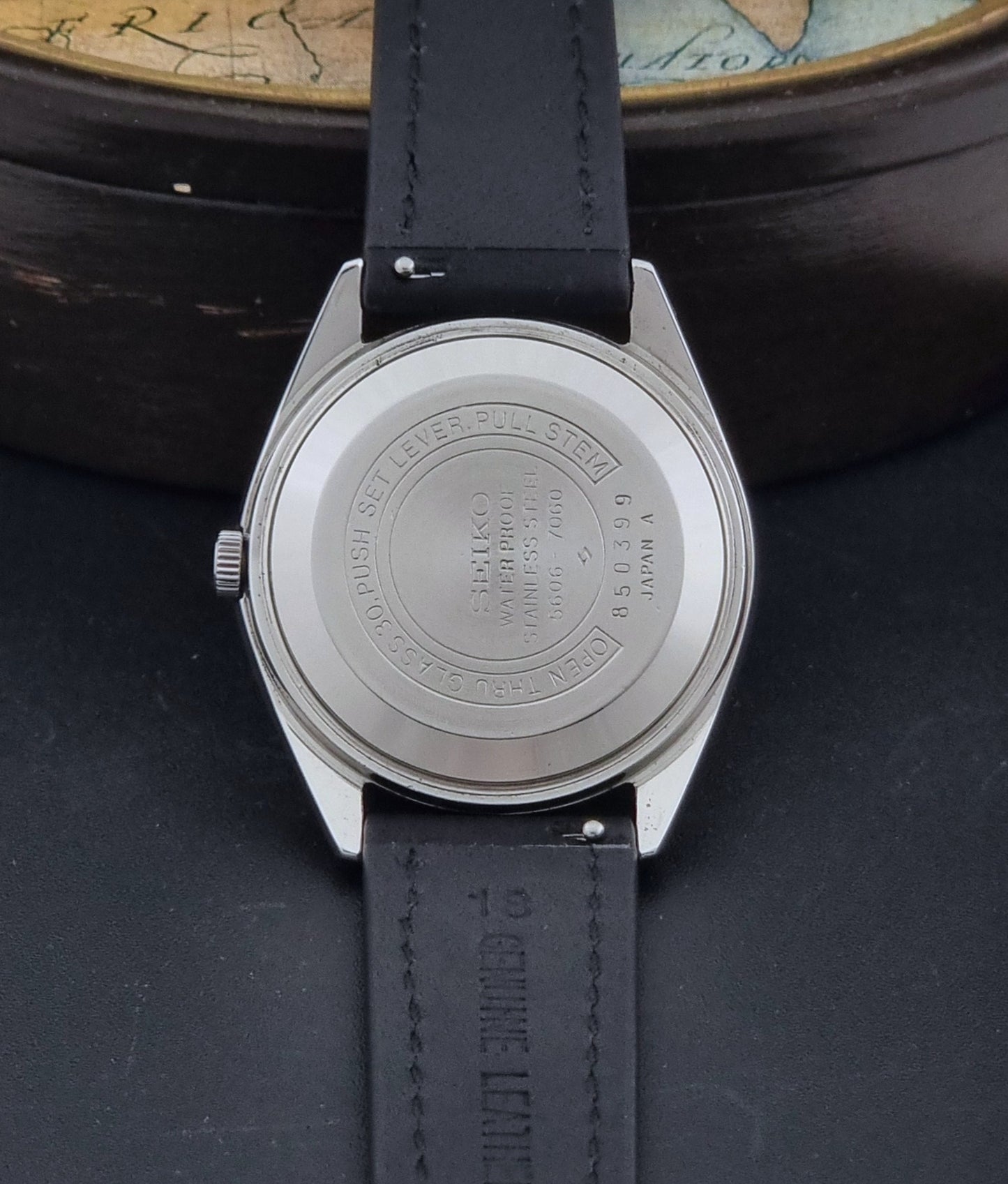 Vintage Seiko Wristwatch 5606-7060 LordMatic Weekdater with black leather strap on a dark gray background case back view