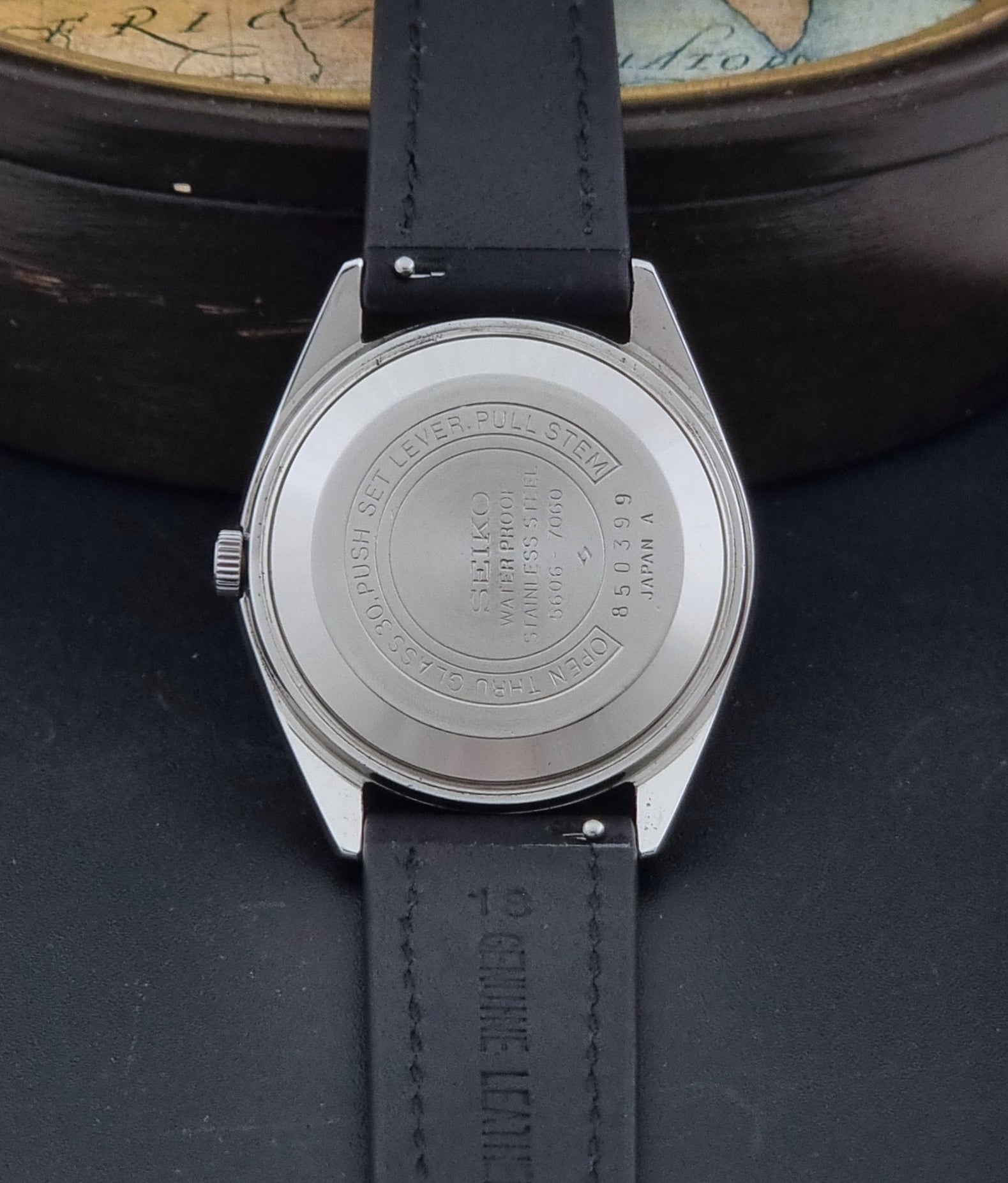 Vintage Seiko Wristwatch 5606-7060 LordMatic Weekdater with black leather strap on a dark gray background case back view