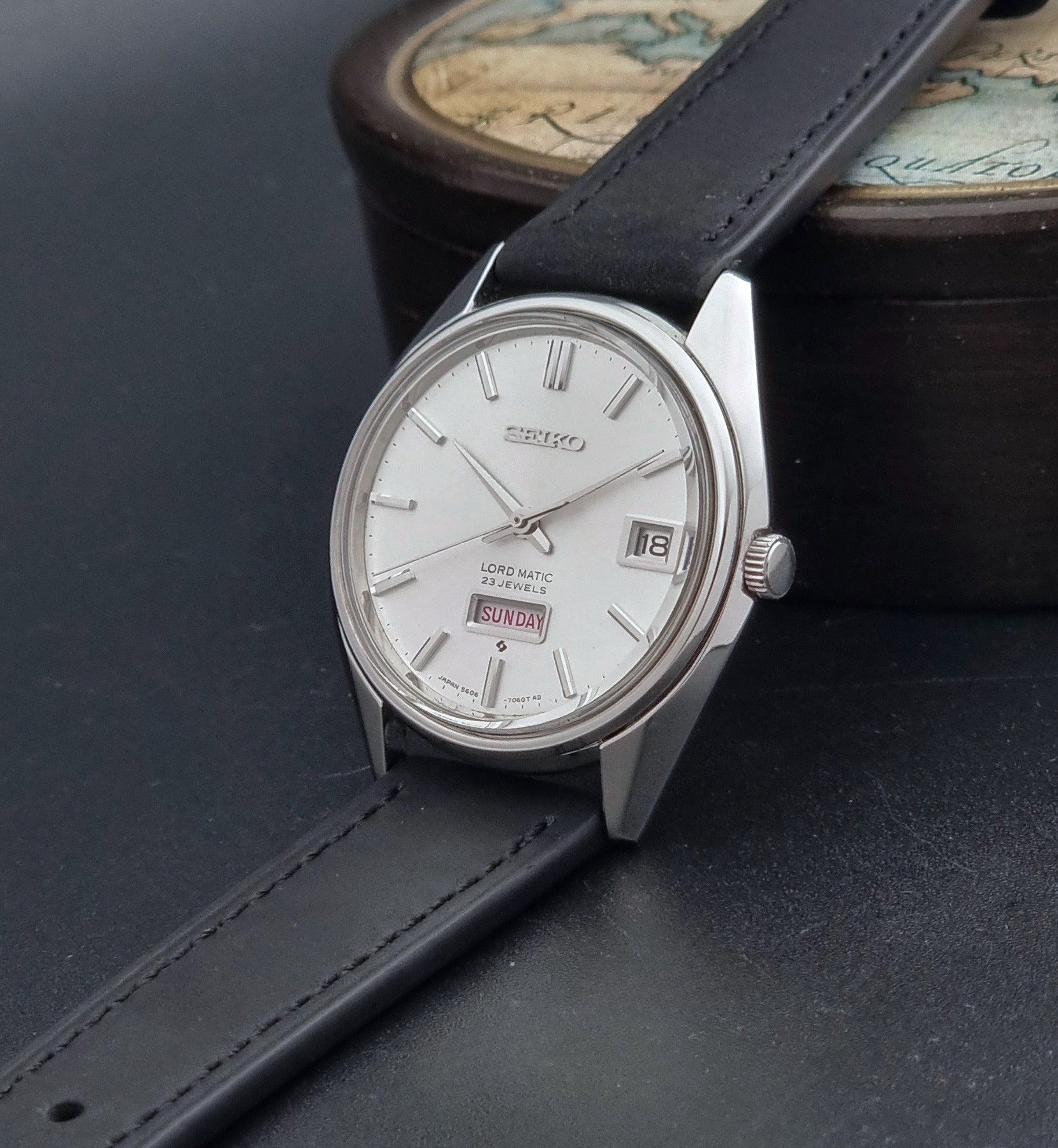 Vintage Seiko Wristwatch 5606-7060 LordMatic Weekdater with black leather strap on a dark gray background crown view