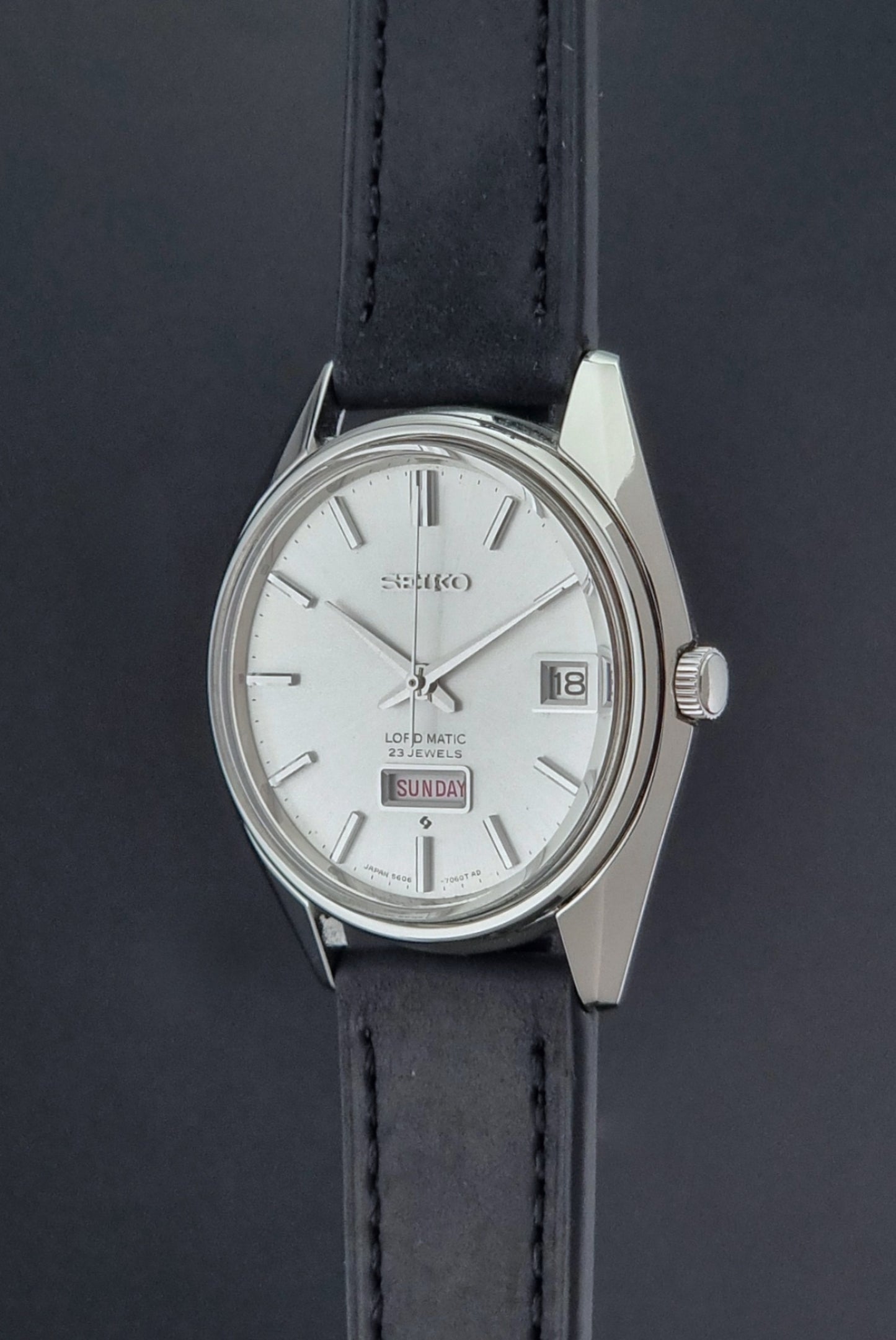 Vintage Seiko Wristwatch 5606-7060 LordMatic Weekdater with black leather strap on a dark gray background crown profile view