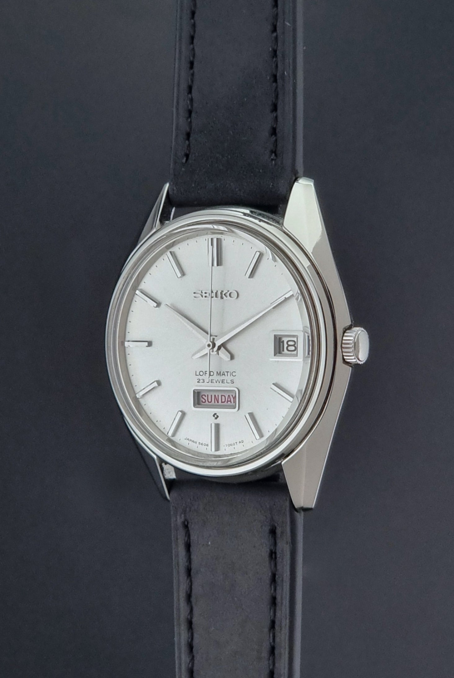Vintage Seiko Wristwatch 5606-7060 LordMatic Weekdater with black leather strap on a dark gray background crown profile view
