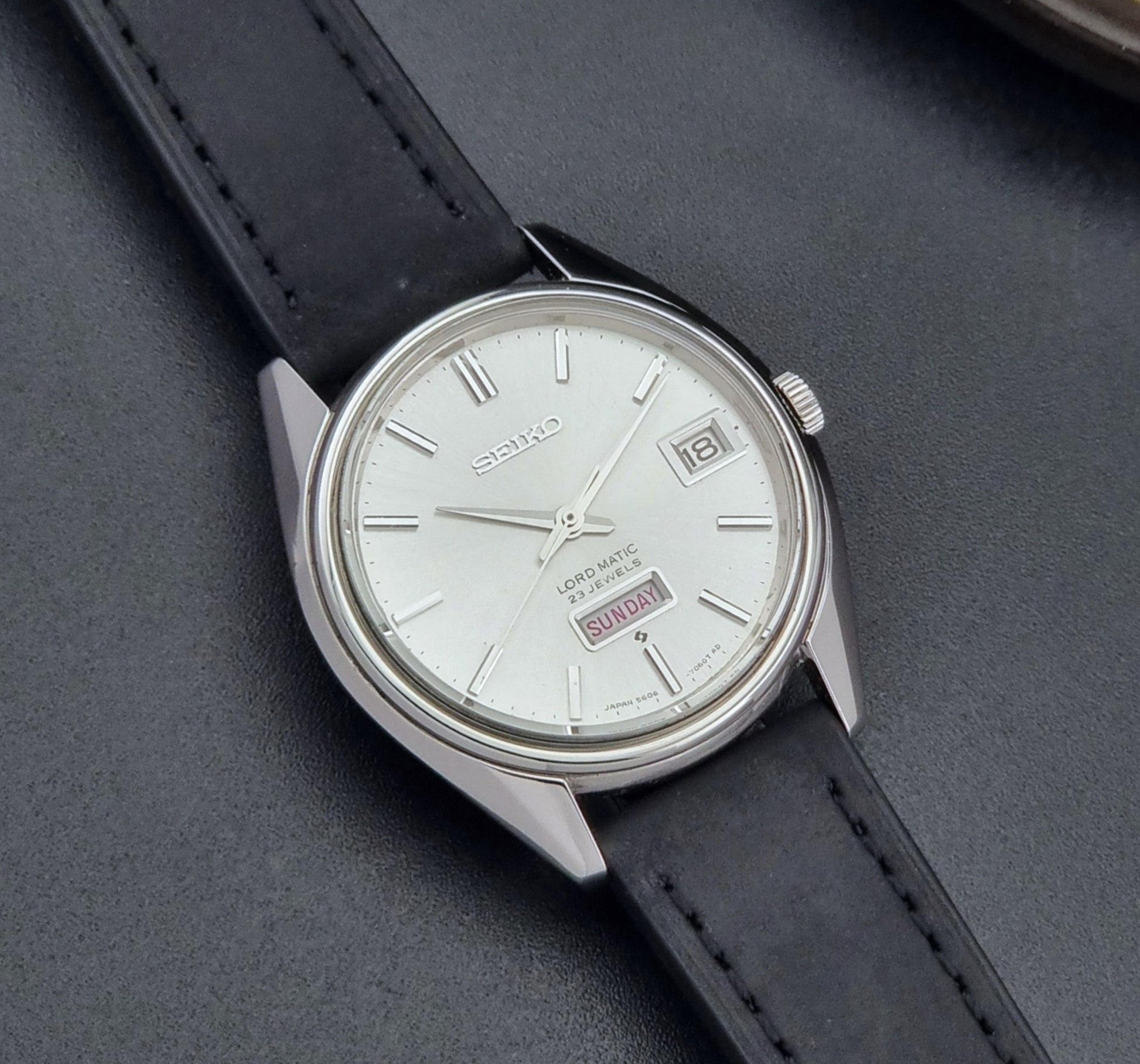 Vintage Seiko Wristwatch 5606-7060 LordMatic Weekdater with black leather strap on a dark gray background close up dial view