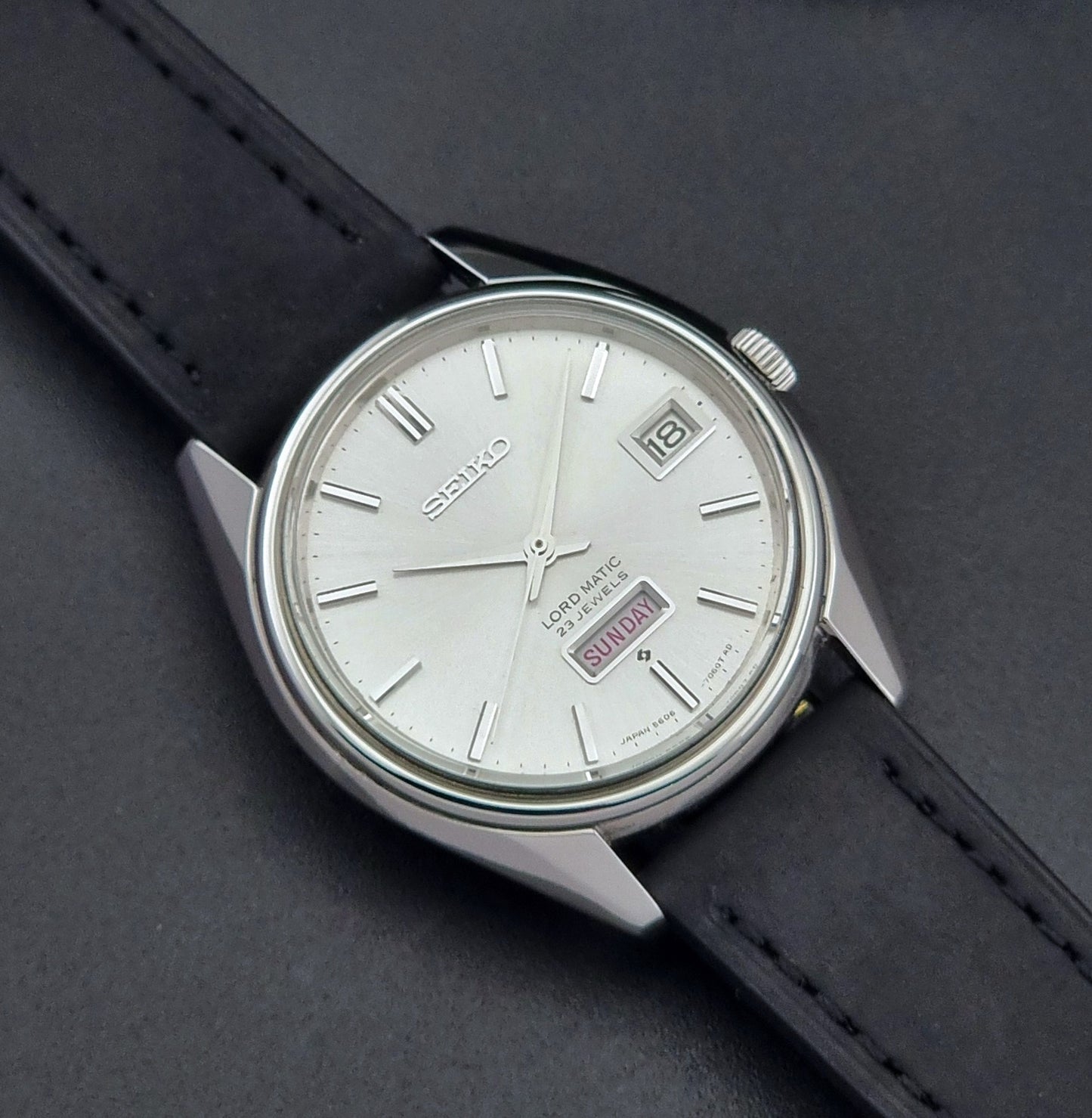 Vintage Seiko Wristwatch 5606-7060 LordMatic Weekdater with black leather strap on a dark gray background front view