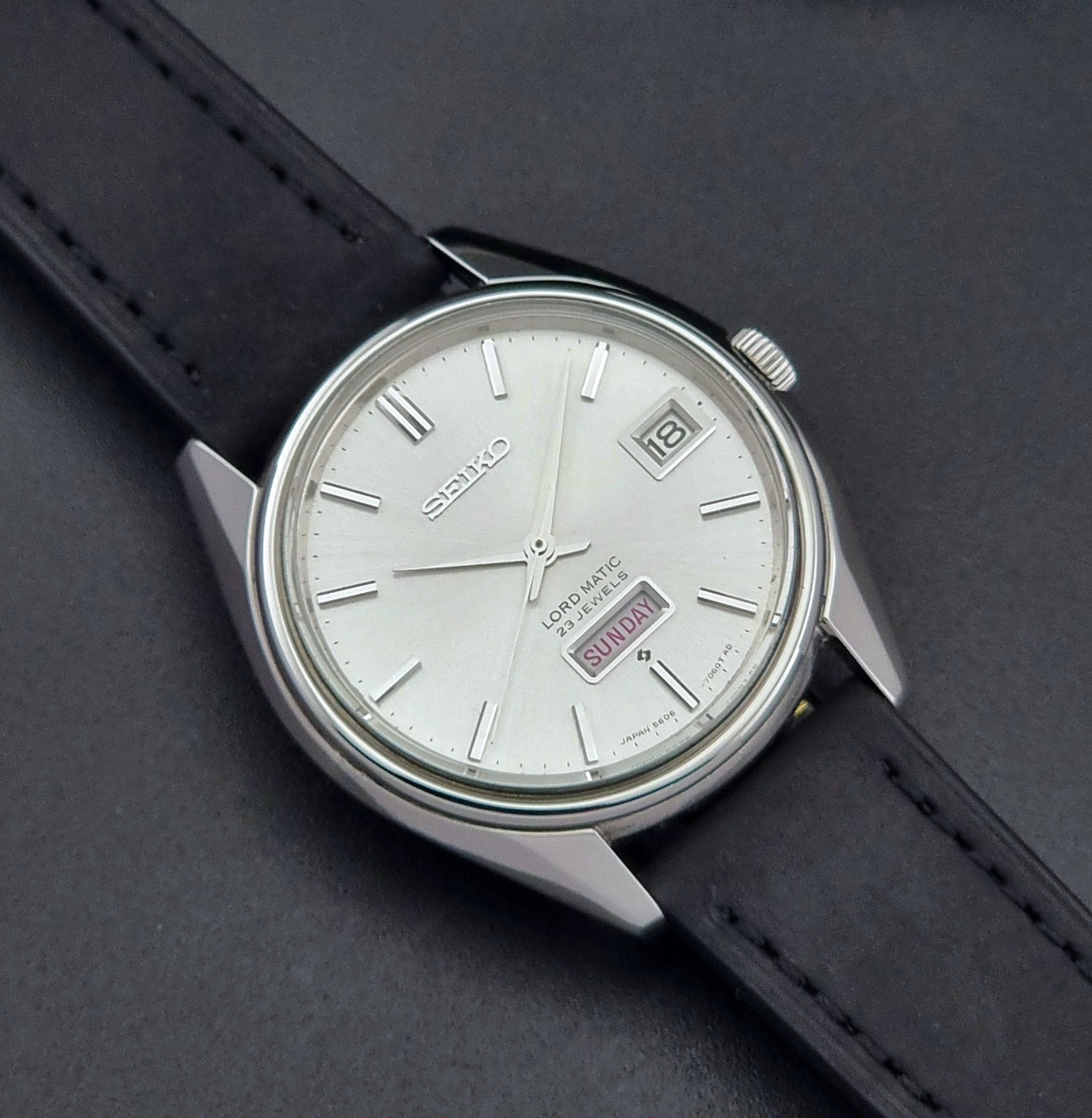 Vintage Seiko Wristwatch 5606-7060 LordMatic Weekdater with black leather strap on a dark gray background front view