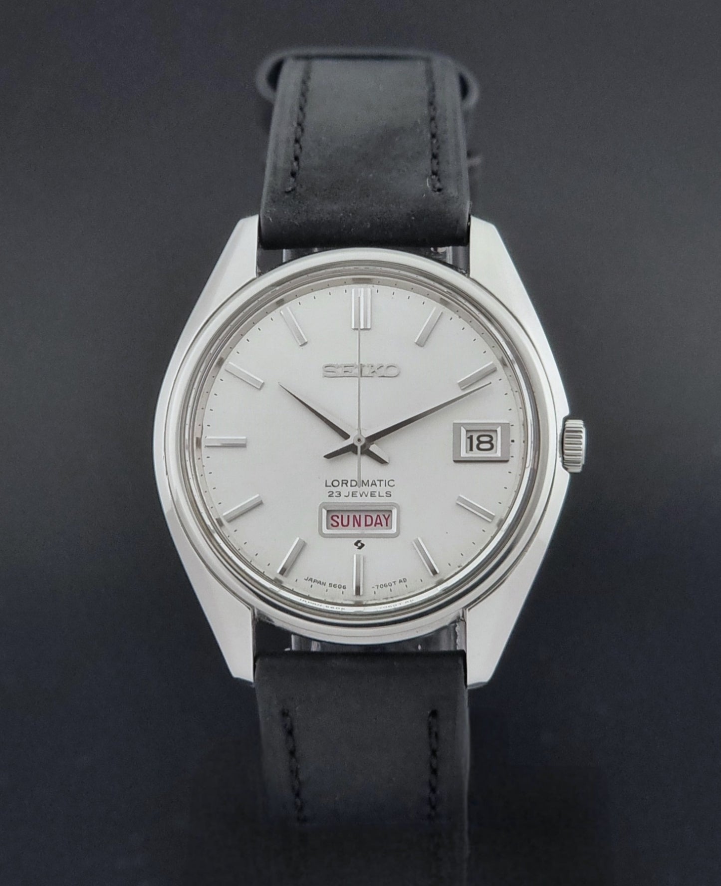 Vintage Seiko Wristwatch 5606-7060 LordMatic Weekdater with black leather strap on a dark gray background close dial view