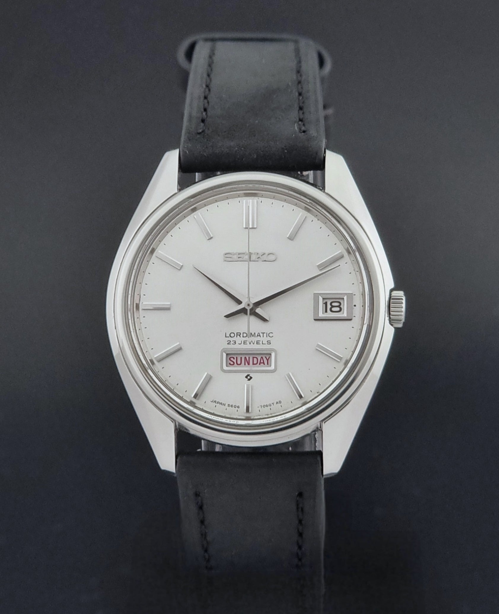 Vintage Seiko Wristwatch 5606-7060 LordMatic Weekdater with black leather strap on a dark gray background close dial view