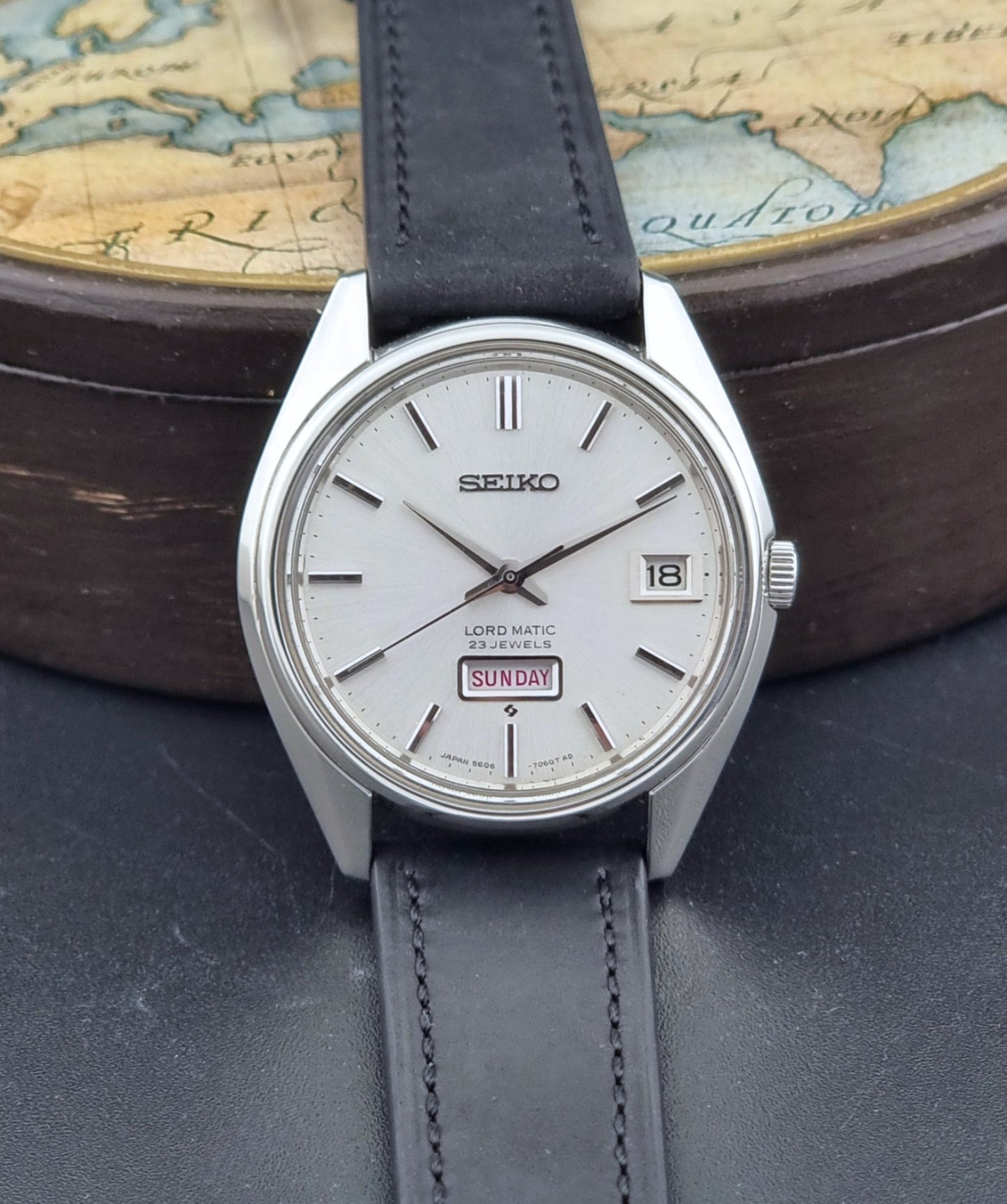Vintage Seiko Wristwatch 5606-7060 LordMatic Weekdater with black leather strap on a dark gray background dial view
