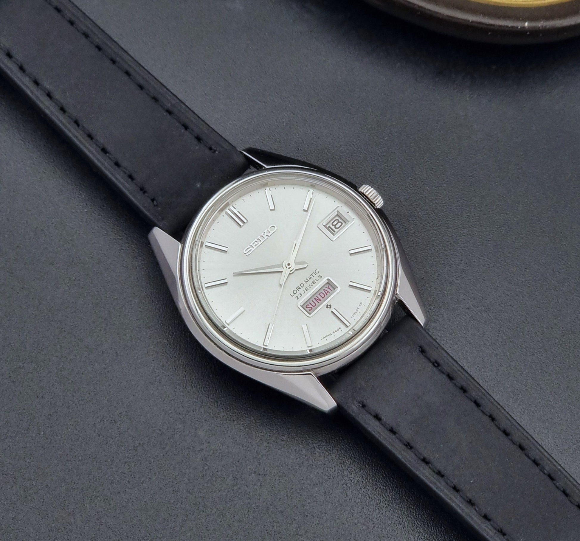 Vintage Seiko Wristwatch 5606-7060 LordMatic Weekdater with black leather strap on a dark gray background dial
