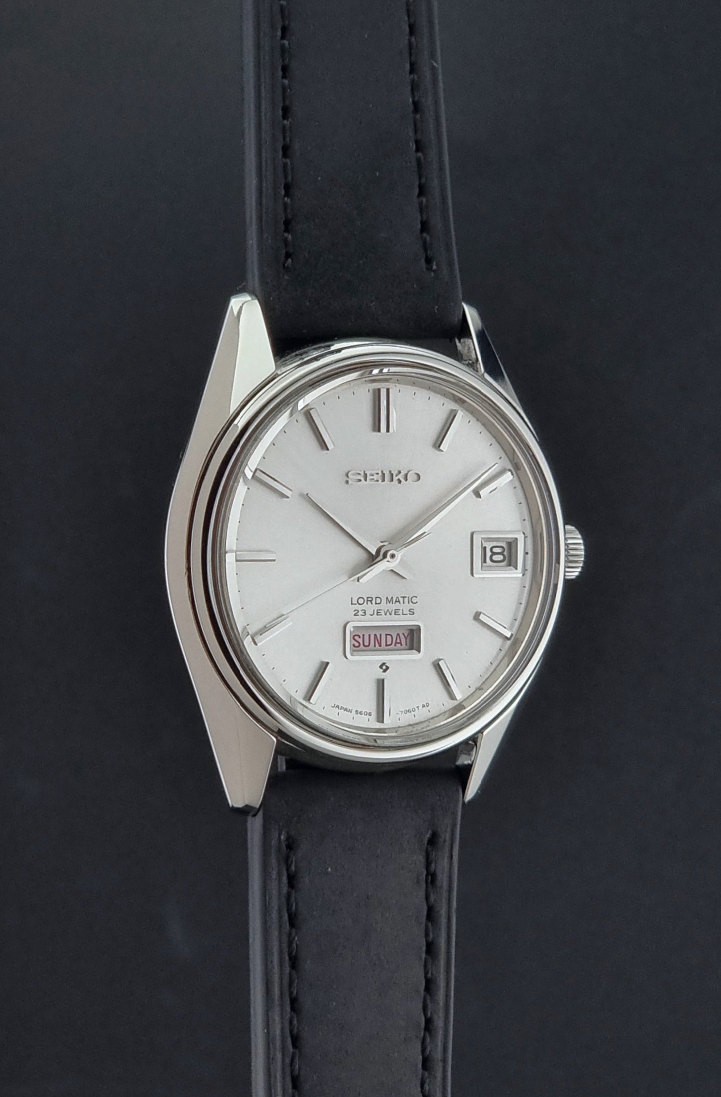 Vintage Seiko Wristwatch 5606-7060 LordMatic Weekdater with black leather strap on a dark gray background side profile view