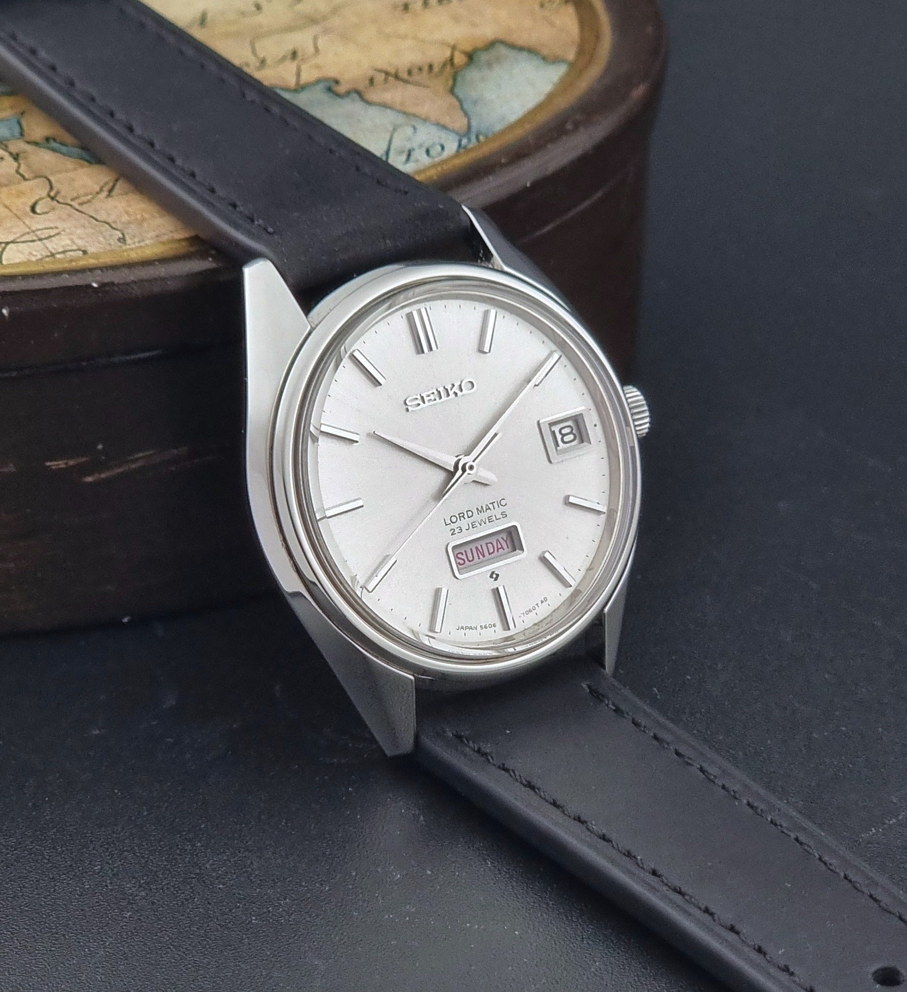 Vintage Seiko Wristwatch 5606-7060 LordMatic Weekdater with black leather strap on a dark gray background side view