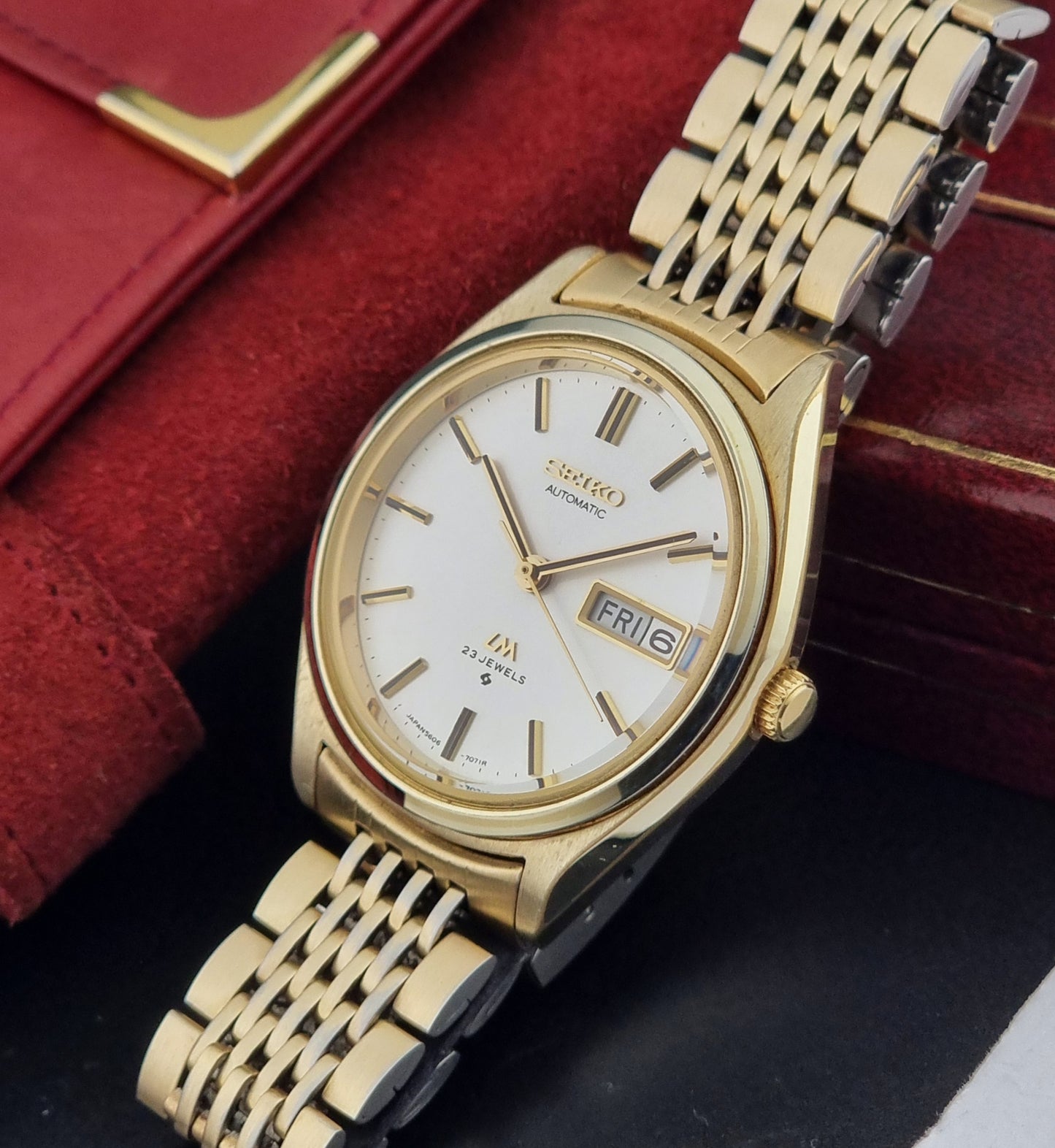 Vintage Seiko LordMatic 5606-7070 Gold wristwatch with a white face on a dark surface crown view