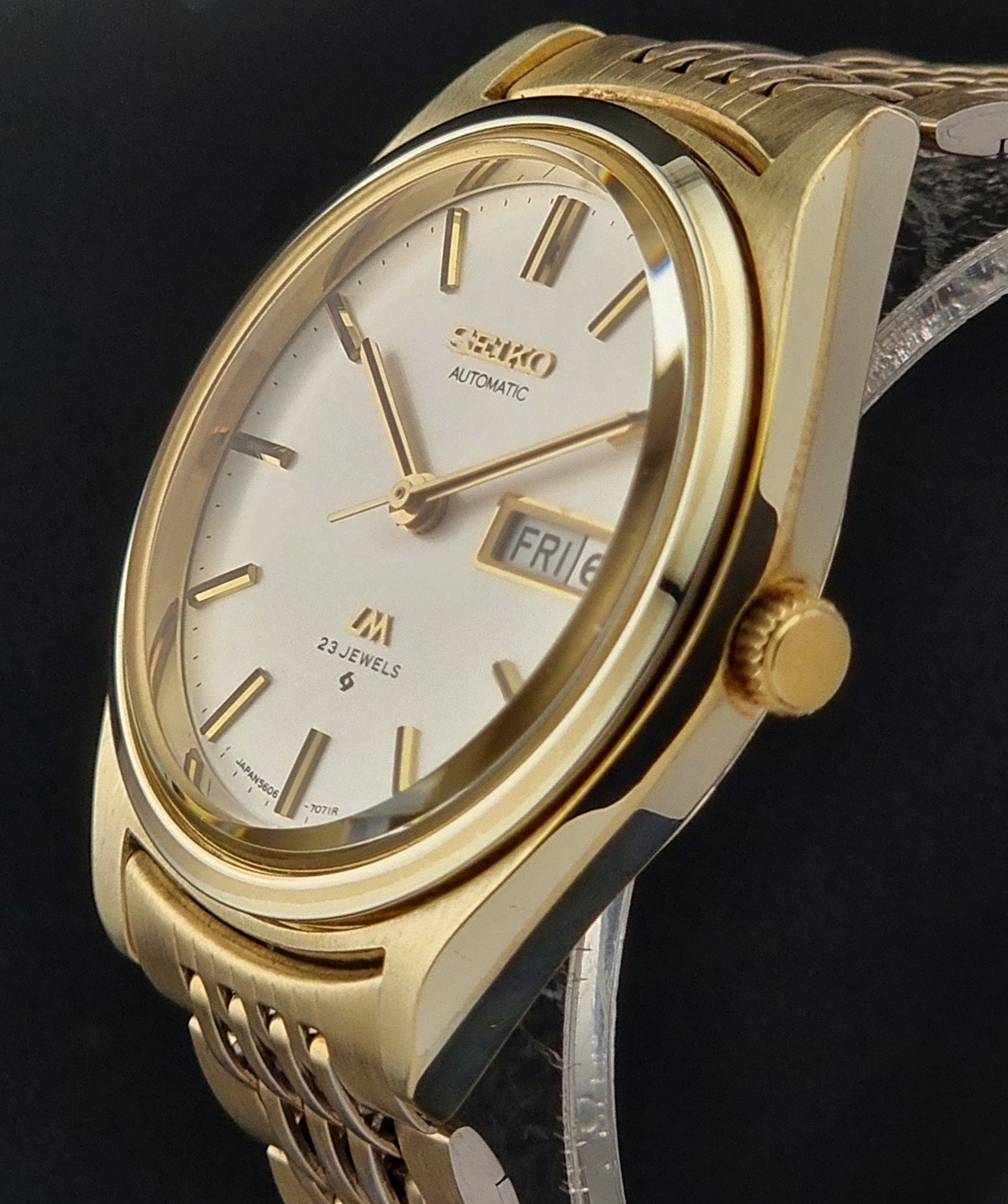 Vintage Seiko LordMatic 5606-7070 Gold wristwatch with a white face on a dark surface crown profile view