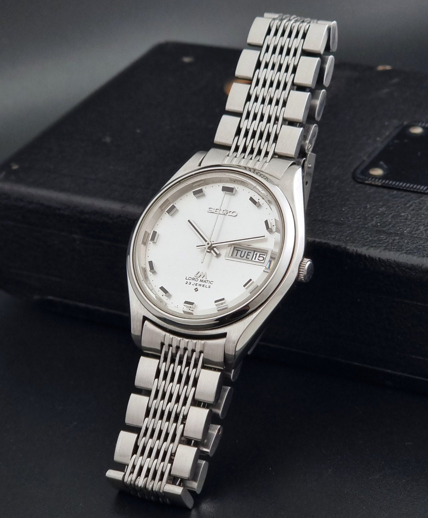 Vintage Seiko 5606-7070 watch LordMatic with a white face on a dark gray background crown view