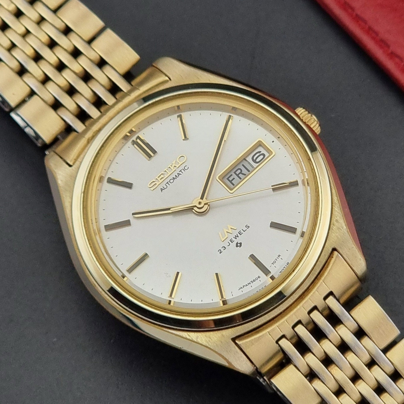 Vintage Seiko LordMatic 5606-7070 Gold wristwatch with a white face on a dark surface close up dial view