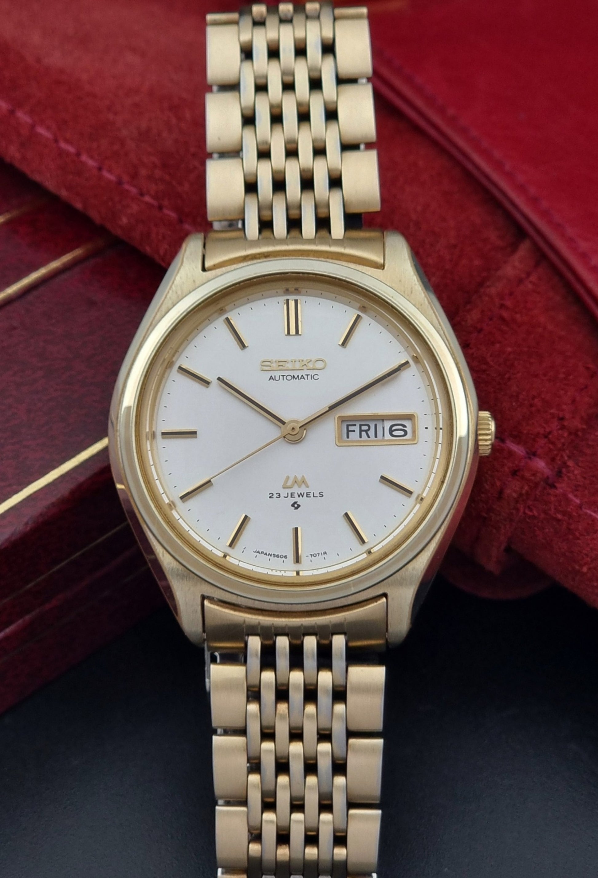 Vintage Seiko LordMatic 5606-7070 Gold wristwatch with a white face on a dark surface dial view