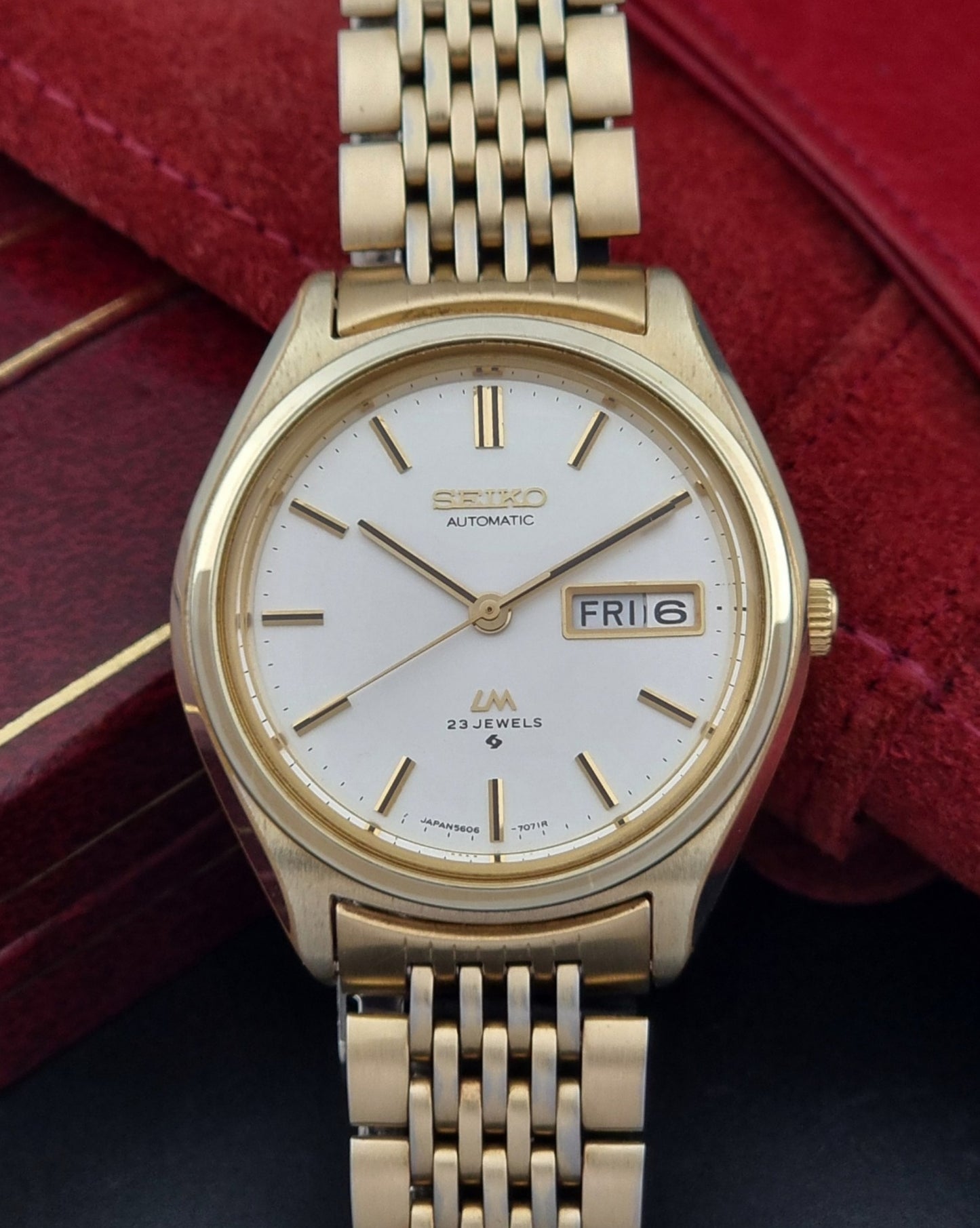 Vintage Seiko LordMatic 5606-7070 Gold wristwatch with a white face on a dark surface close up dial view