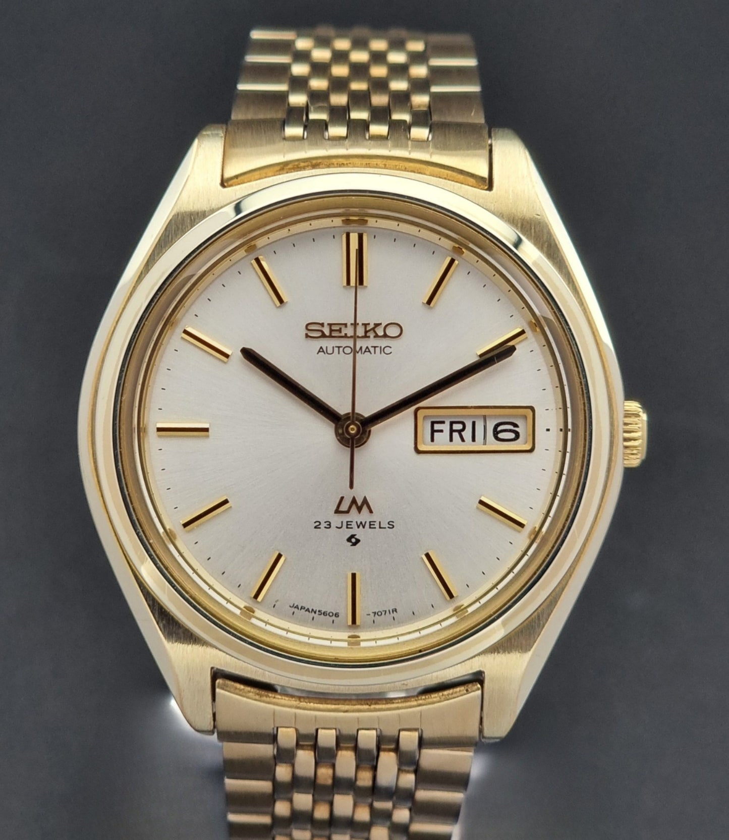 Vintage Seiko LordMatic 5606-7070 Gold wristwatch with a white face on a dark surface close dial view