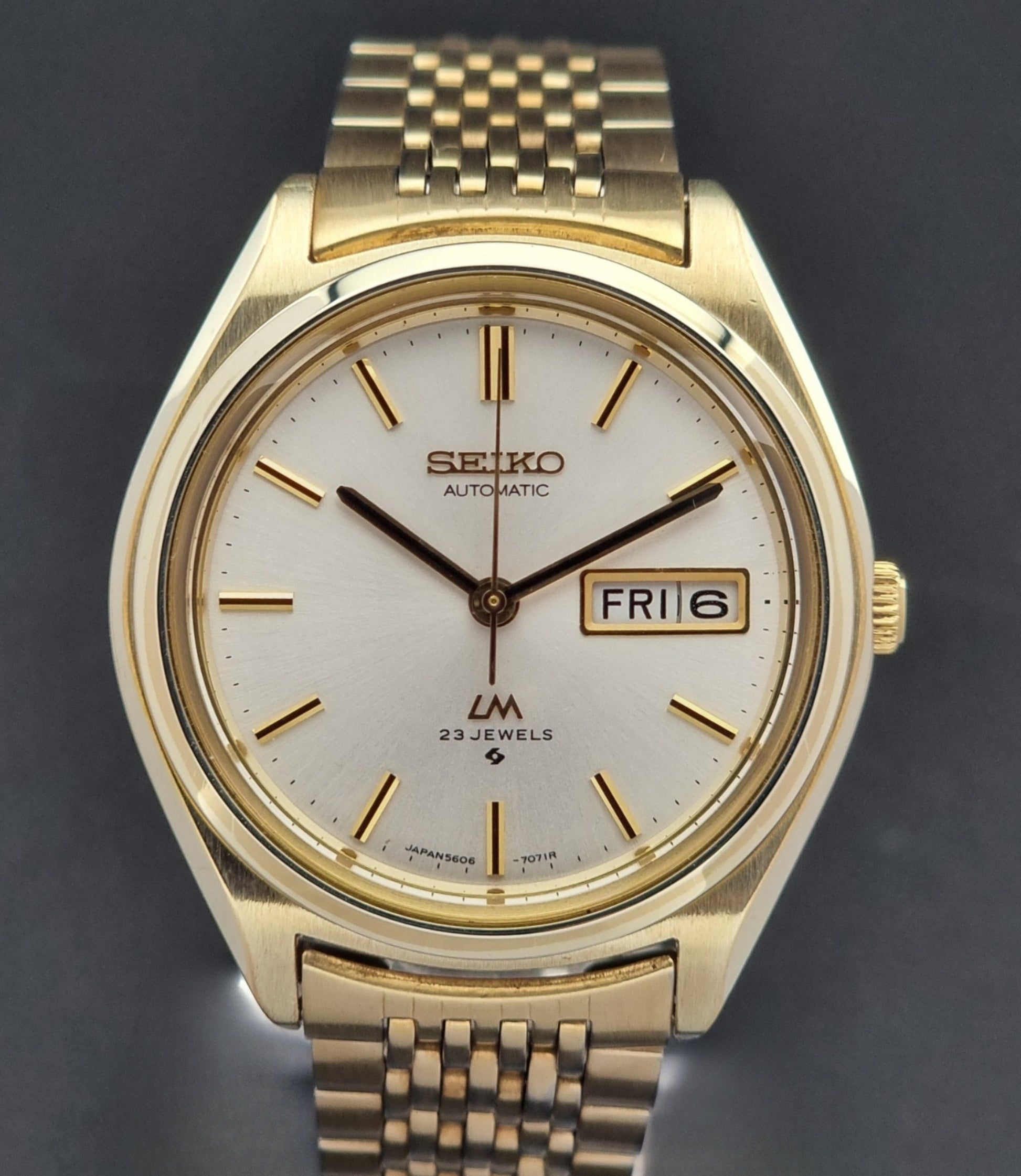 Vintage Seiko LordMatic 5606-7070 Gold wristwatch with a white face on a dark surface close dial view