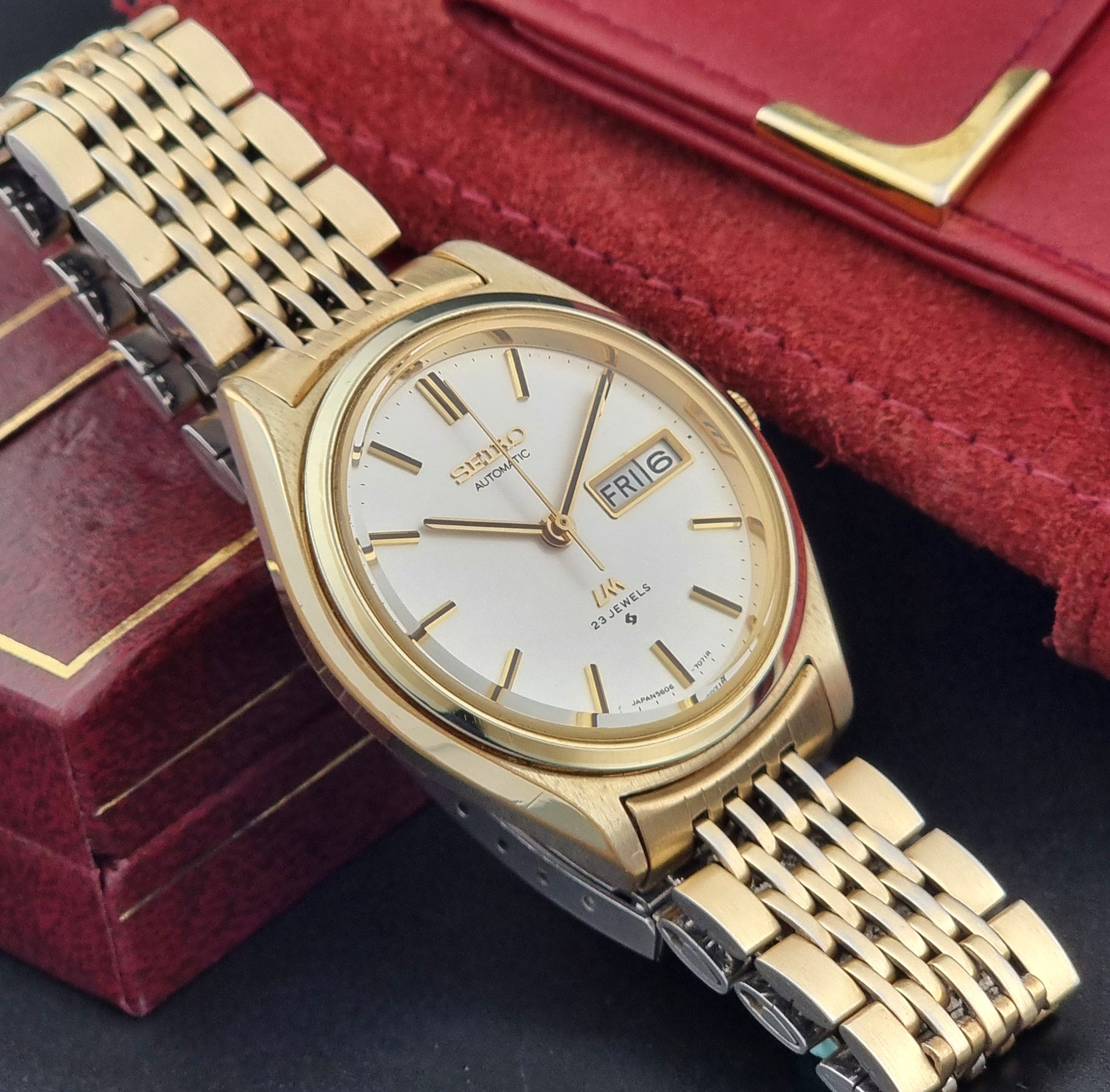 Vintage Seiko LordMatic 5606-7070 Gold wristwatch with a white face on a dark surface side view