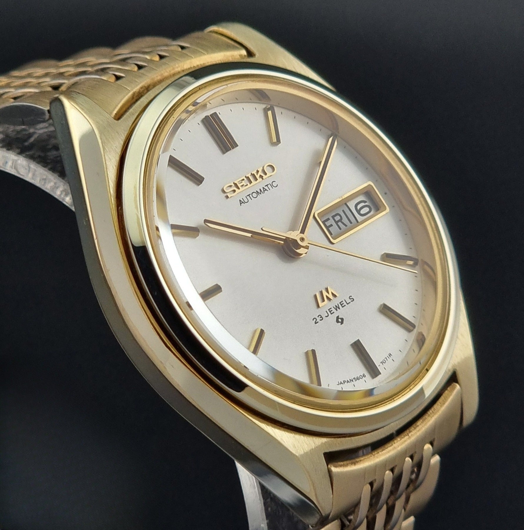 Vintage Seiko LordMatic 5606-7070 Gold wristwatch with a white face on a dark surface side profile view