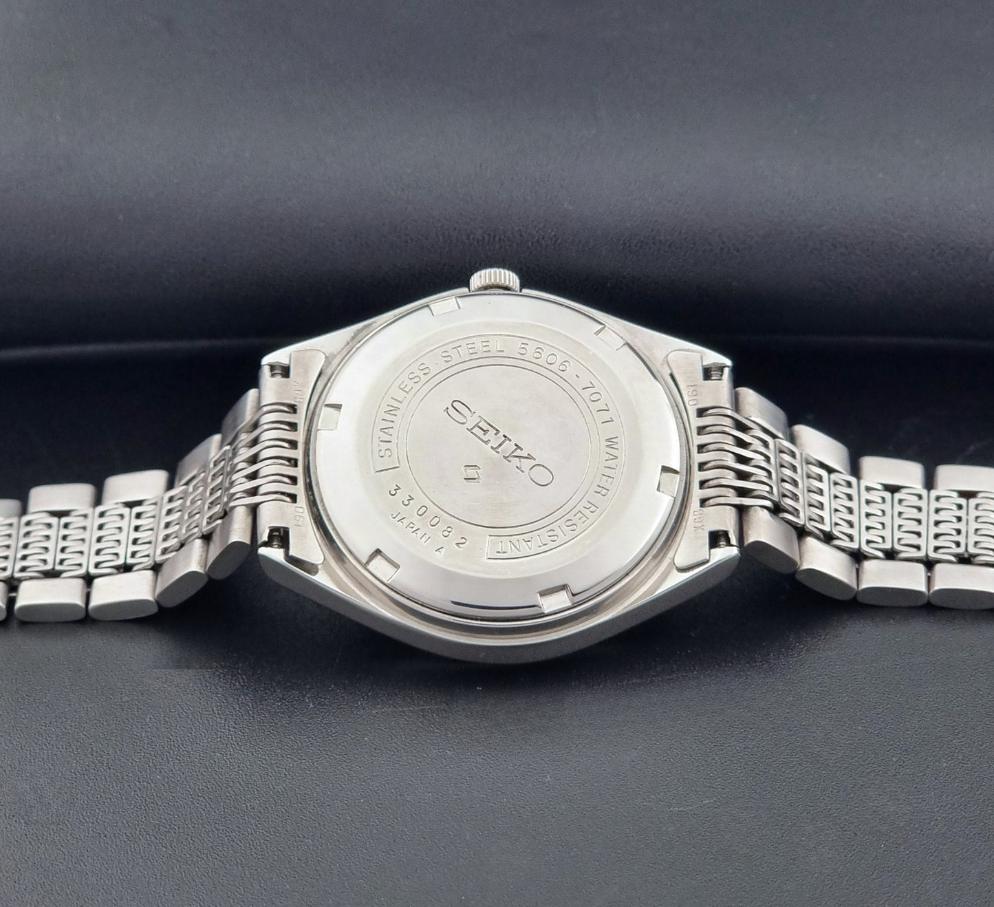 Vintage Seiko 5606-7071 LordMatic wristwatch with a metallic band on a dark gray background case back view