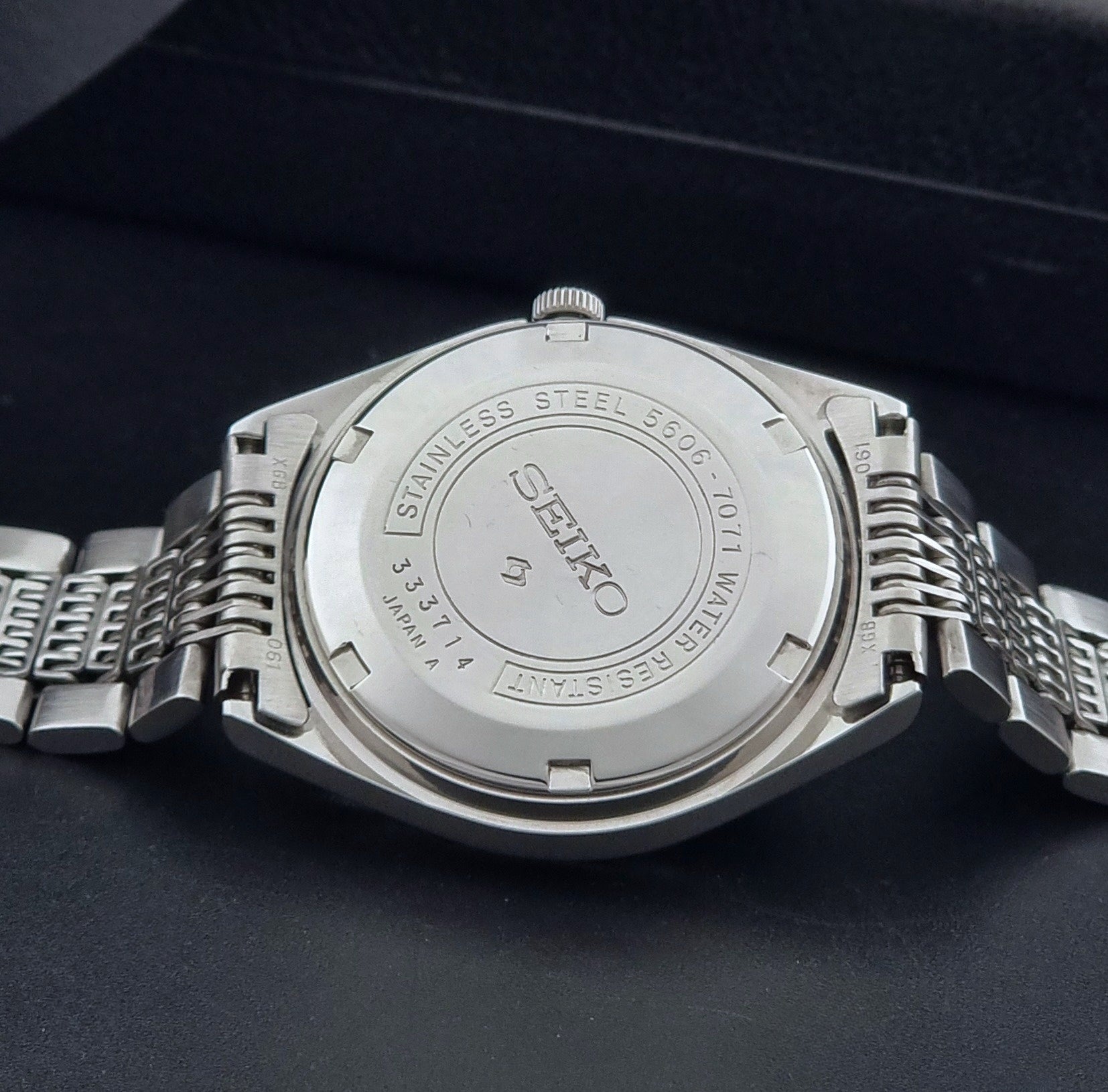Vintage Seiko Wristwatch 5606-7071  with a metallic band on a dark background case back view