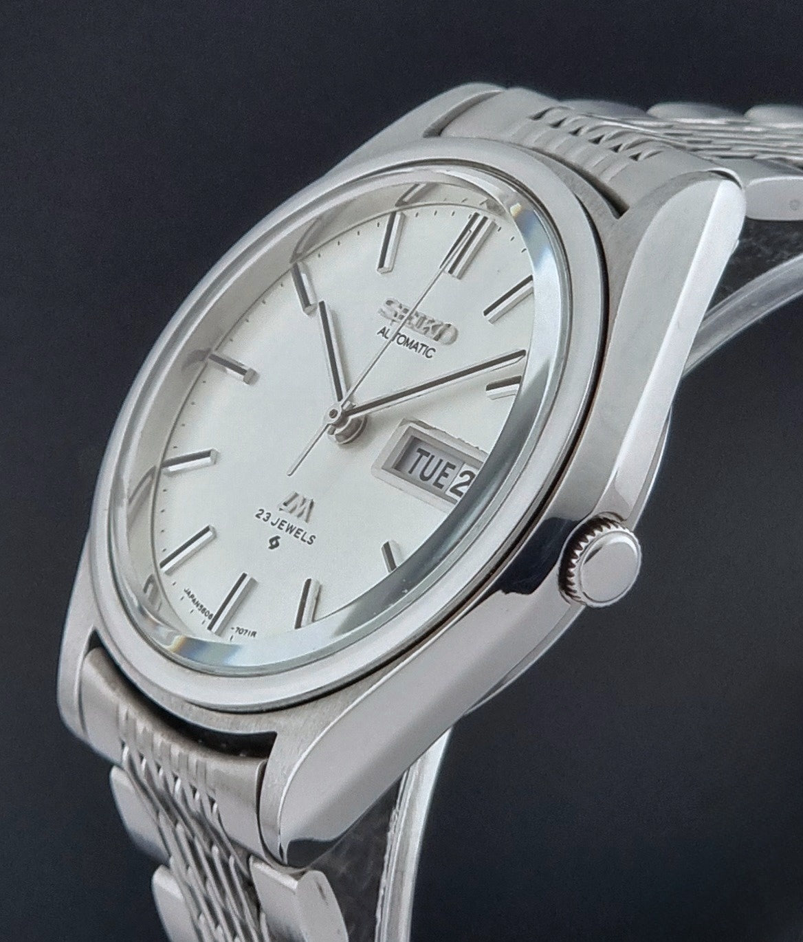 Vintage Seiko Wristwatch 5606-7071  with a metallic band on a dark background crown profile view